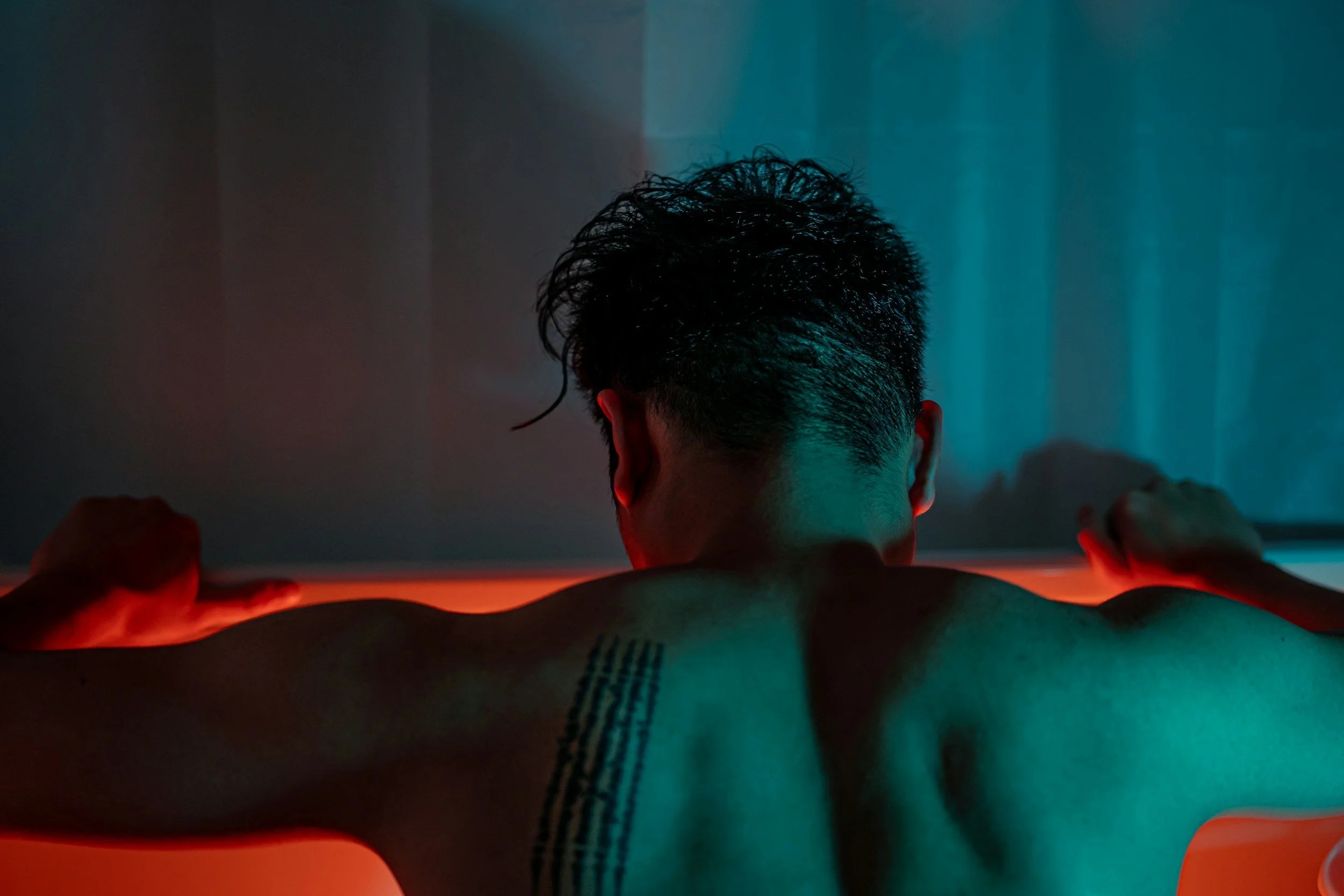 Intimacy coach session imagery for penis owners, featuring a person with shoulder tattoos in ambient lighting to represent nervous system regulation.