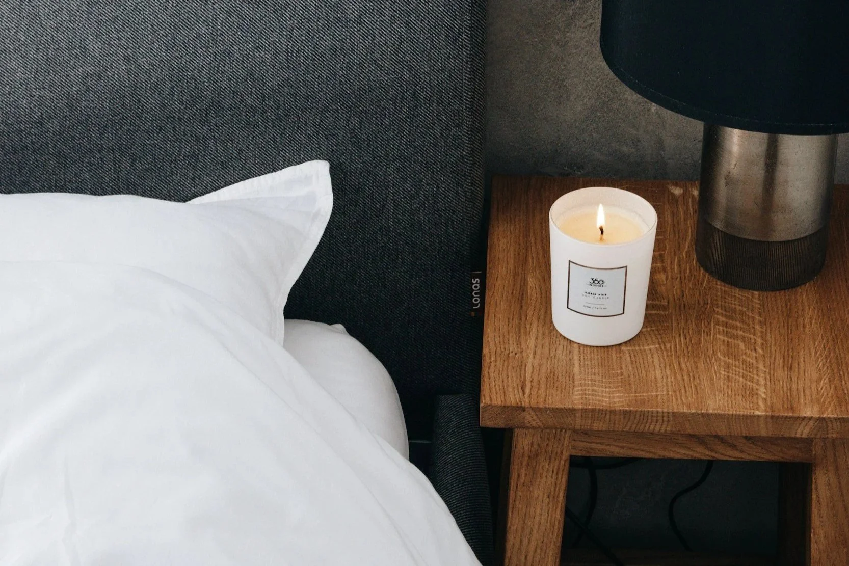 Cozy bedroom setting with crisp white linen sheets, wooden bedside table, and a lit candle for solo somatic practice.