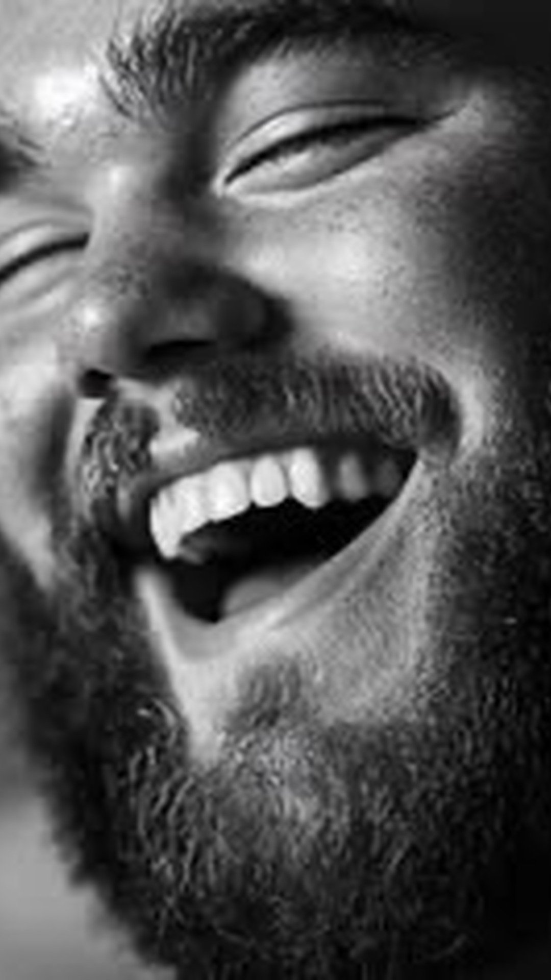 A close-up black and white portrait of a bearded man laughing joyfully, symbolizing sexual vitality and emotional freedom.