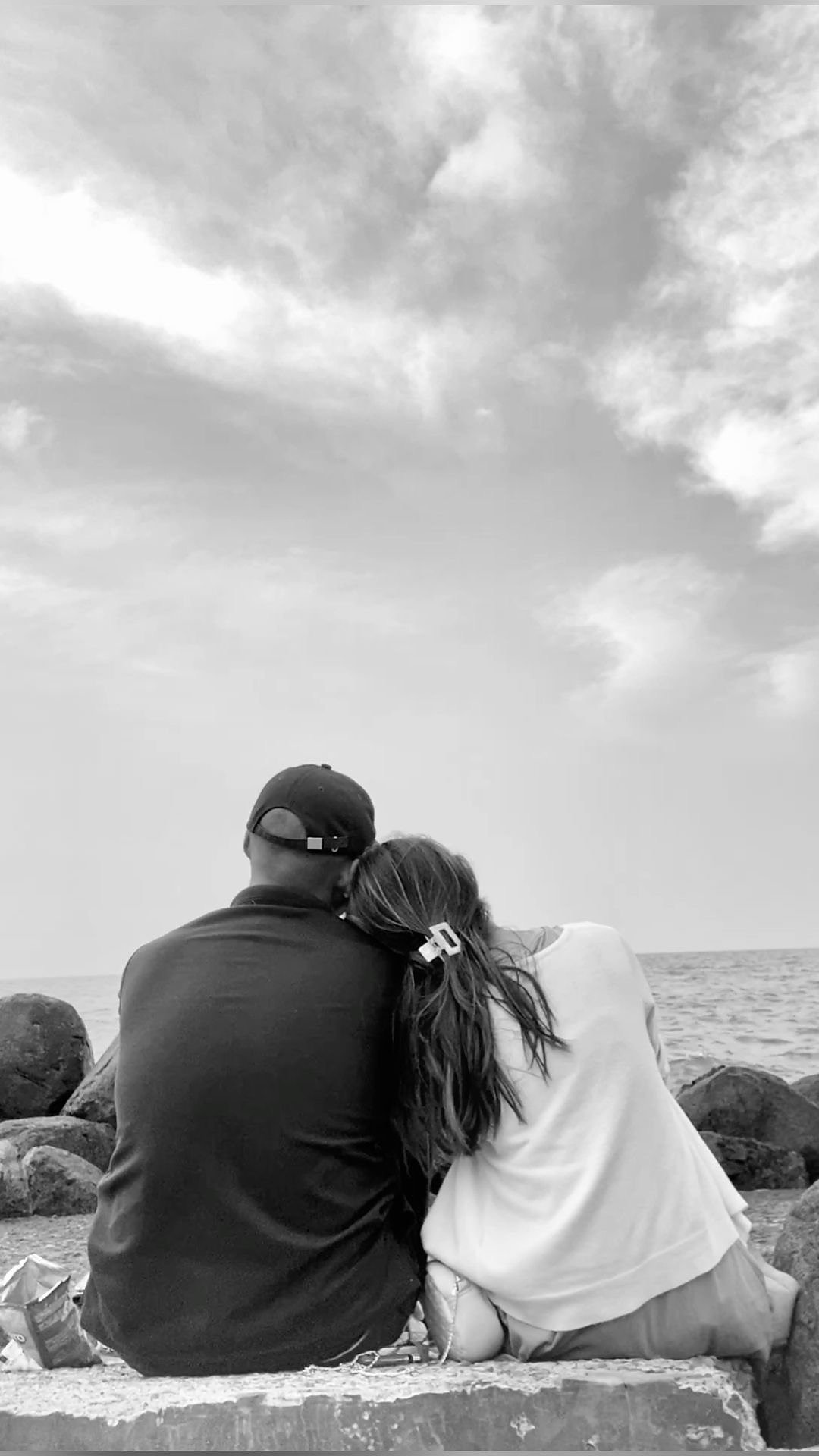 Couple sitting together on a rocky shore looking at the ocean, building deeper connection through relational coaching.