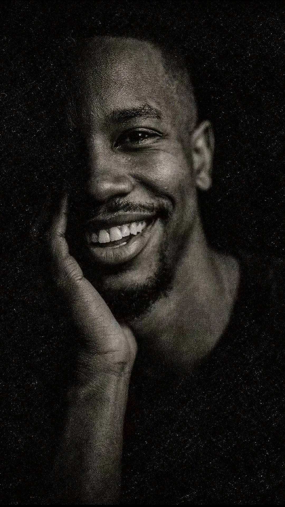 A smiling man in black and white resting his hand on his jaw, representing emotional openness and confidence.