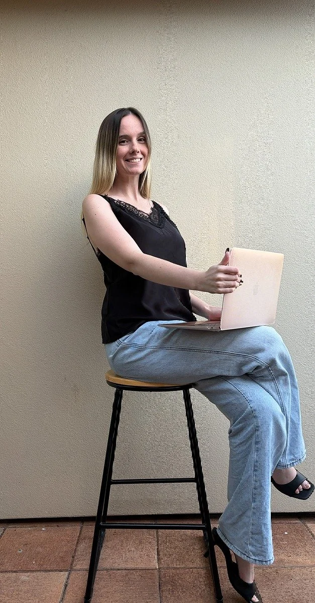 One of NZ's top sex coaches, Michaela Tutty sitting on a stool with her laptop ready to have Zoom calls with men to improve their intimacy.