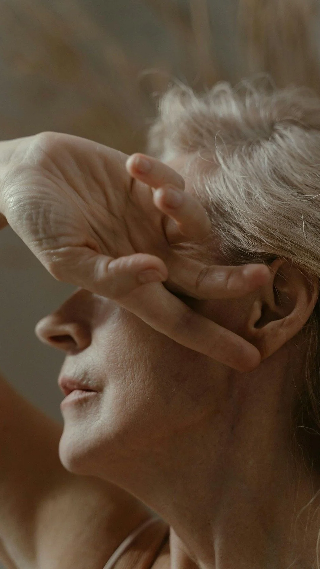 A mature woman softly resting her hand over her face, representing presence, emotional healing, and somatic sex coaching for vulva owners.