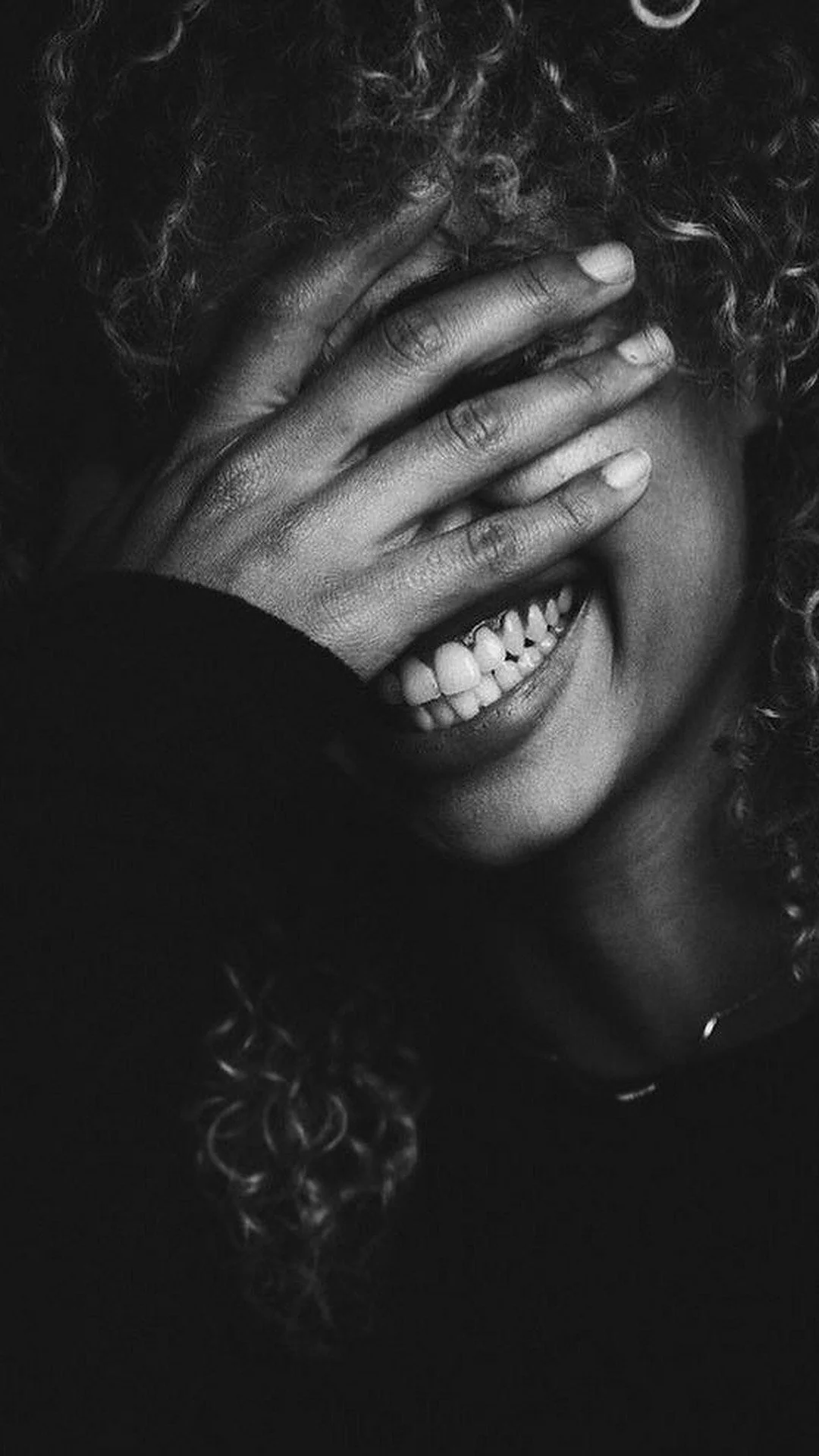 A woman smiling softly while gently shielding her face, illustrating intimacy and emotional vulnerability.