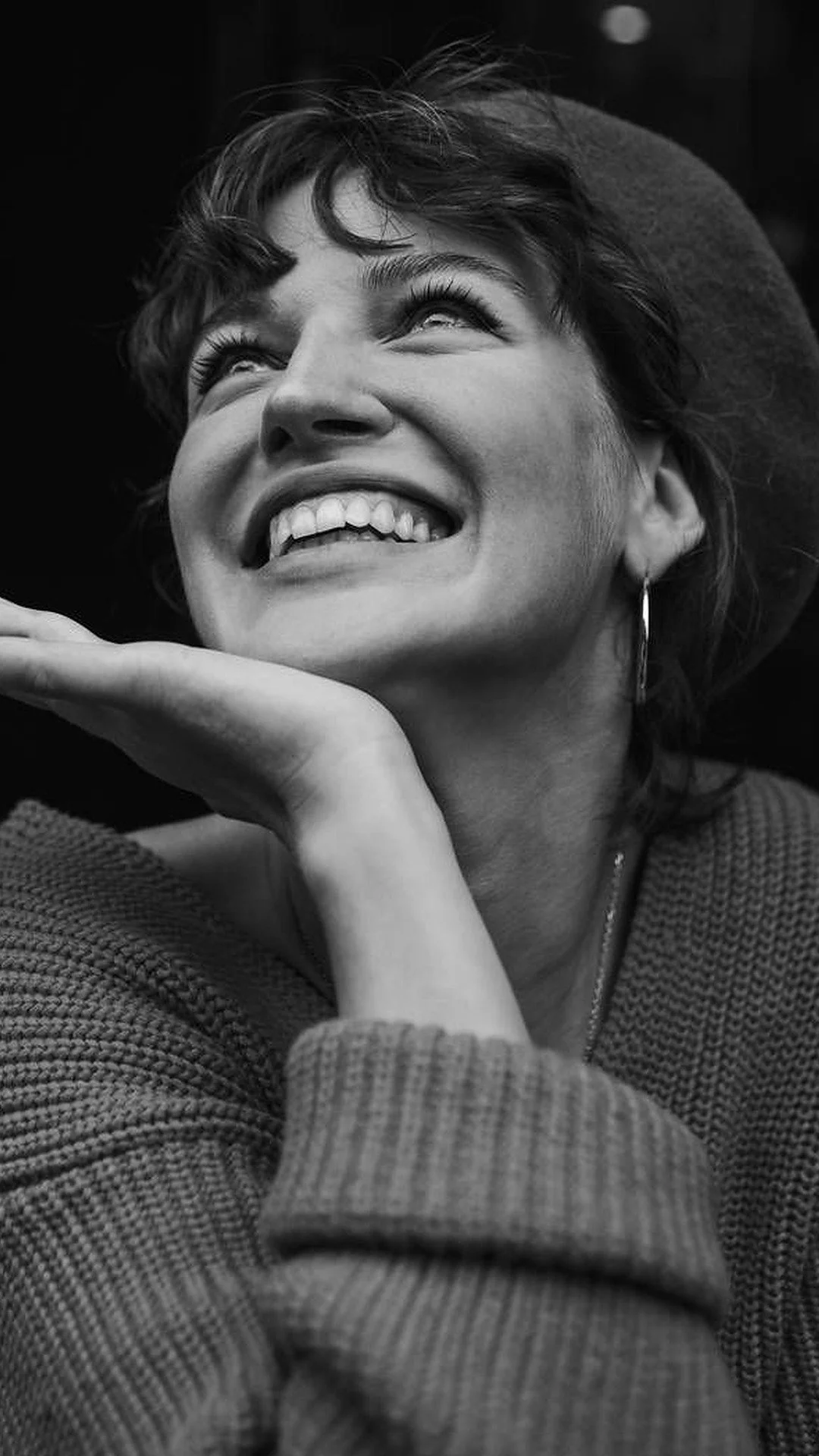 A woman wearing a beret resting her hands under her chin with a radiant, confident smile.