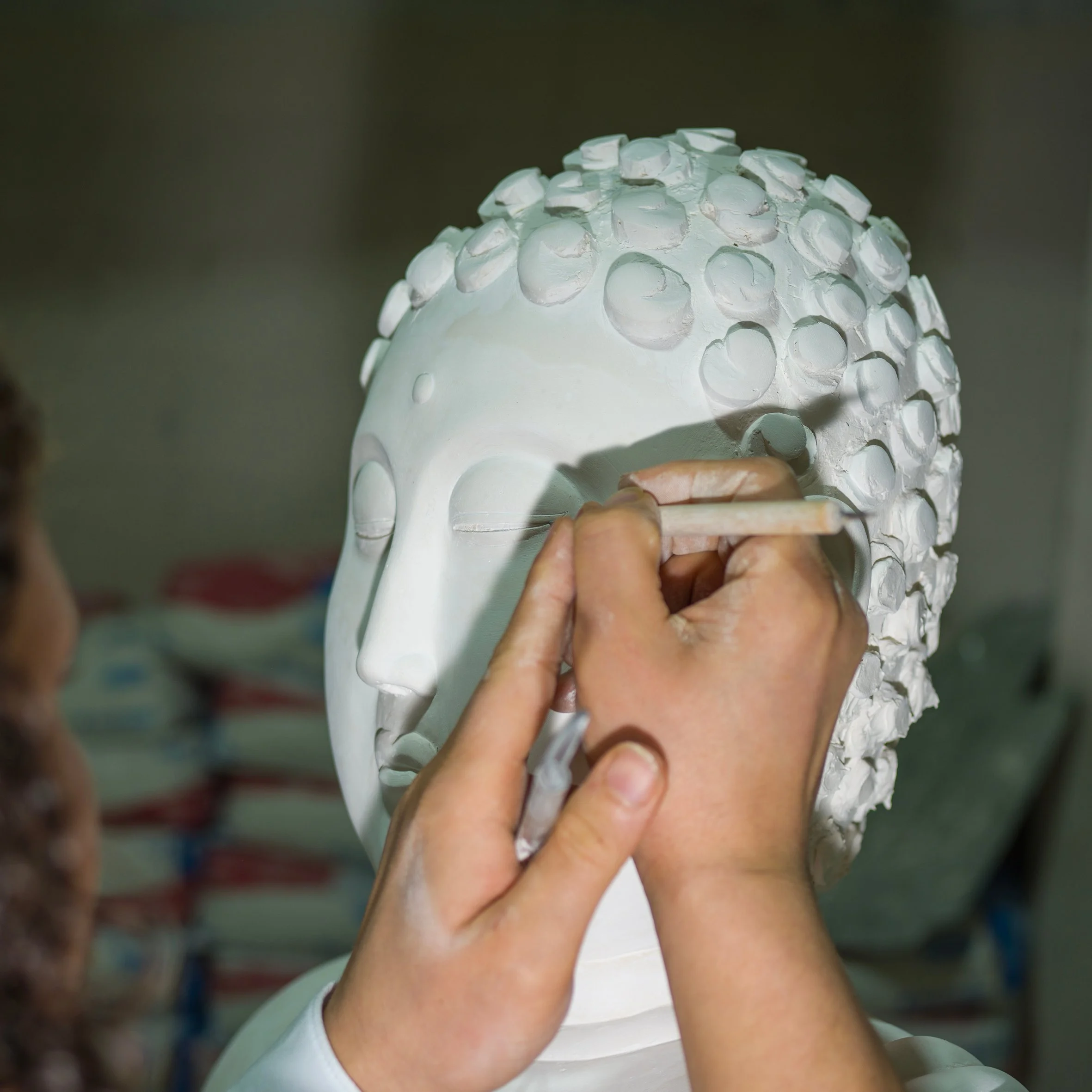 Une personne peint un visage de statue en pierre blanche, en ajoutant des détails au niveau de l'œil, avec des décorations en relief sur la tête.