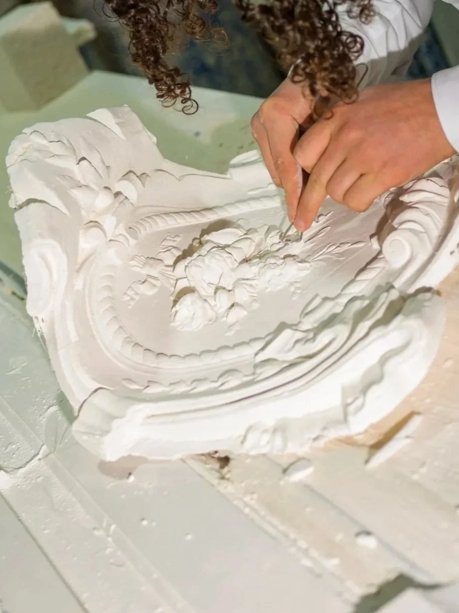 Une personne sculpte un décor en plâtre blanc avec des outils d'artisanat.