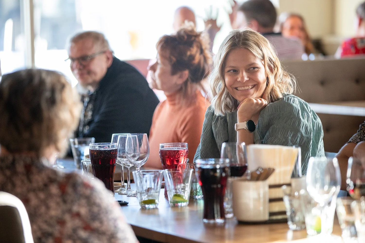 Nuori nainen hymyilee ja istuu ravintolassa seurueen kanssa.