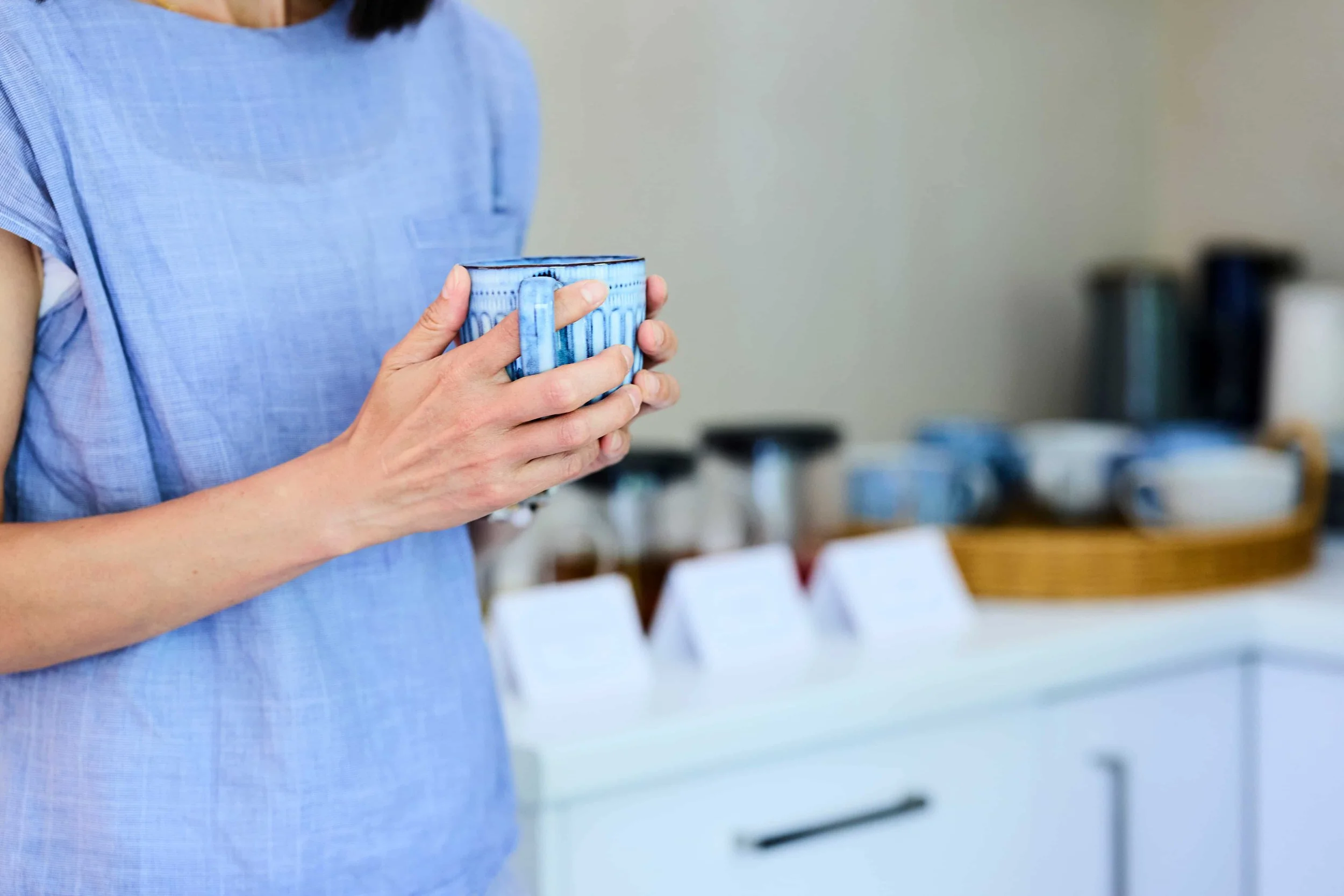 A woman holding a blue ceramic mug in a kitchen or dining area.