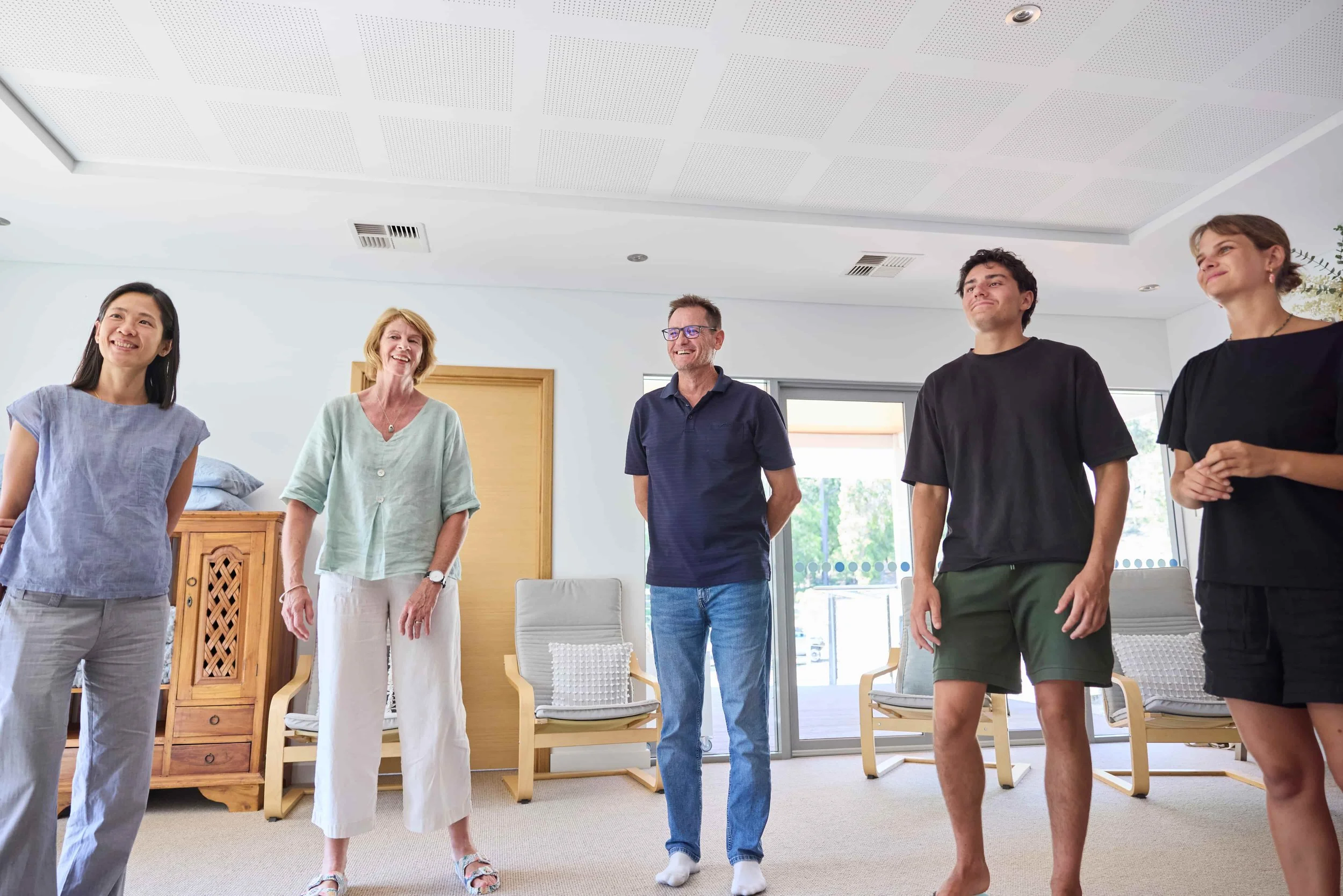 Group of five people standing and smiling in a bright, modern room with large windows and casual seating, performing practical mindfulness and mental wellness tools