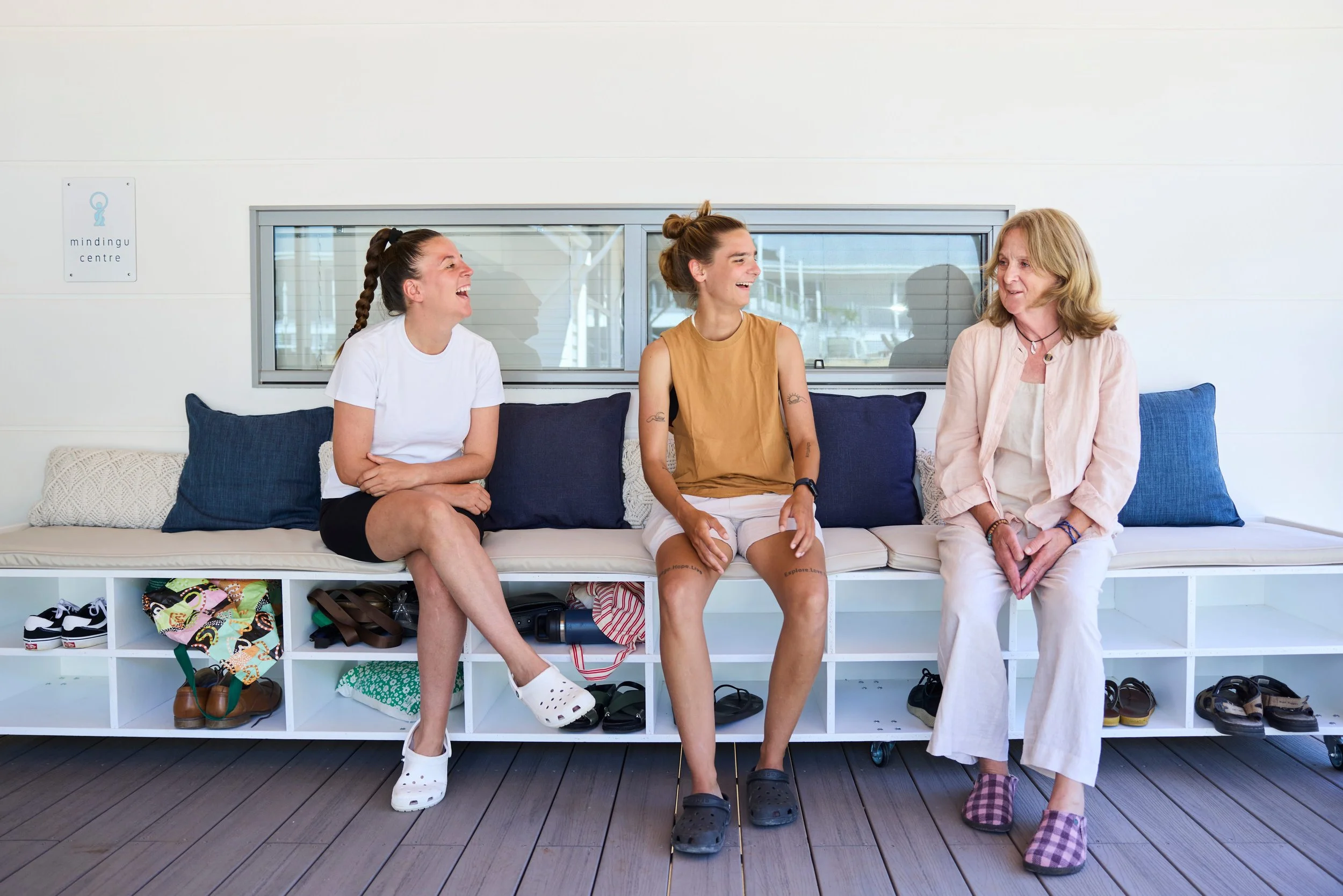 Three women sitting on a bench in a bright indoor space, laughing and engaging in conversation.