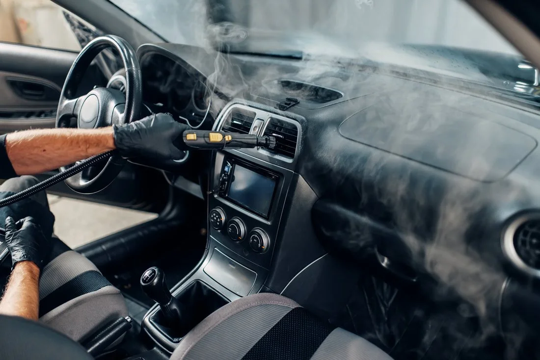 Person using a steam cleaning device to remove smoke or residue from the dashboard and vents inside a car.