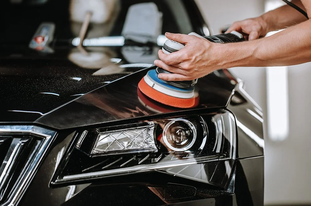 Person polishing the black car's headlight with a polish machine and foam pad.