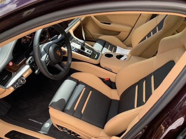 Interior of a luxury car with beige and black seats, a steering wheel, center console with gear shifter, cup holders, and papers on the passenger seat.