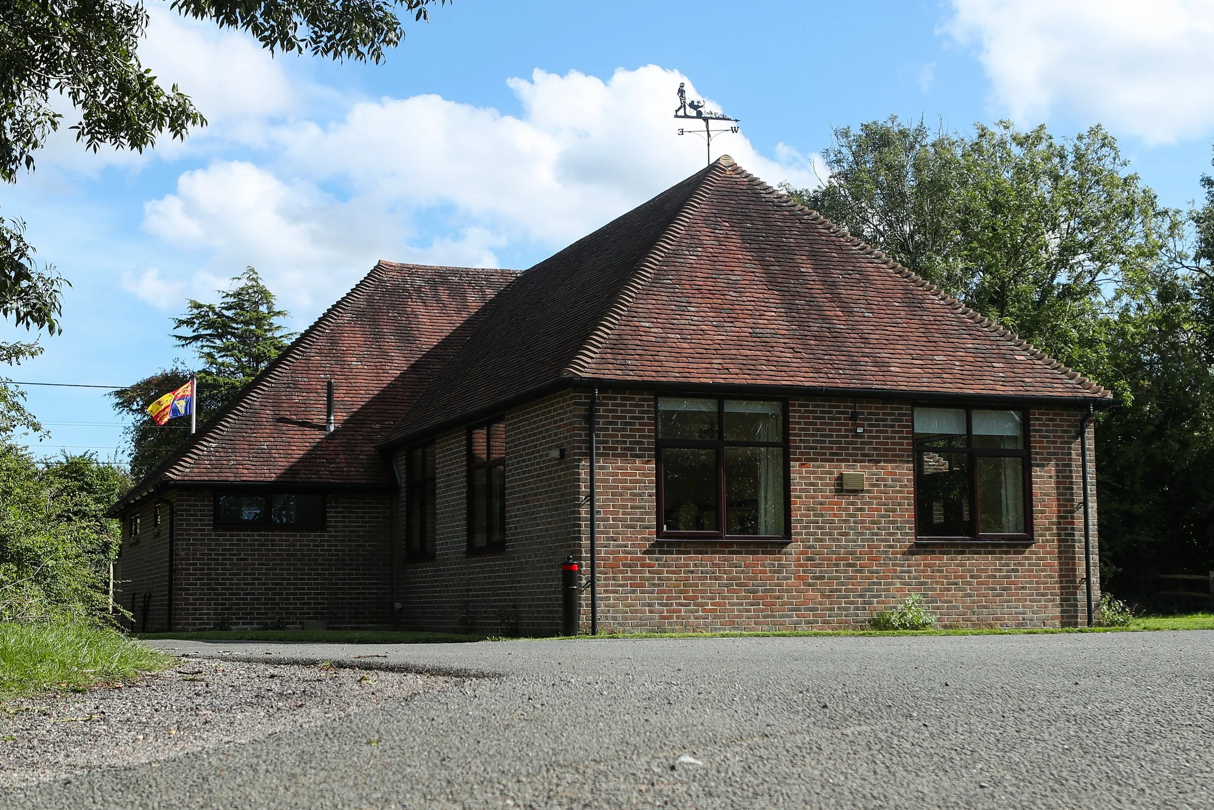 A brick house with a sloped tile roof, surrounded by trees, under a partly cloudy sky.