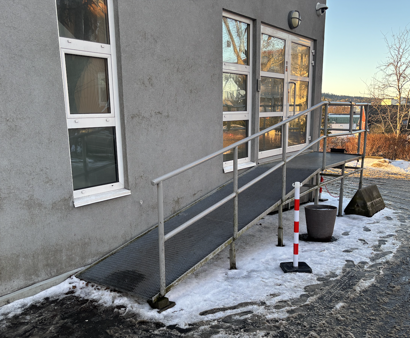 Rampe utenfor offentlig bygg, Rampen er bratt, har en kant i starten, og mangler tilstrekkelig størrelse på repos utenfor døren.