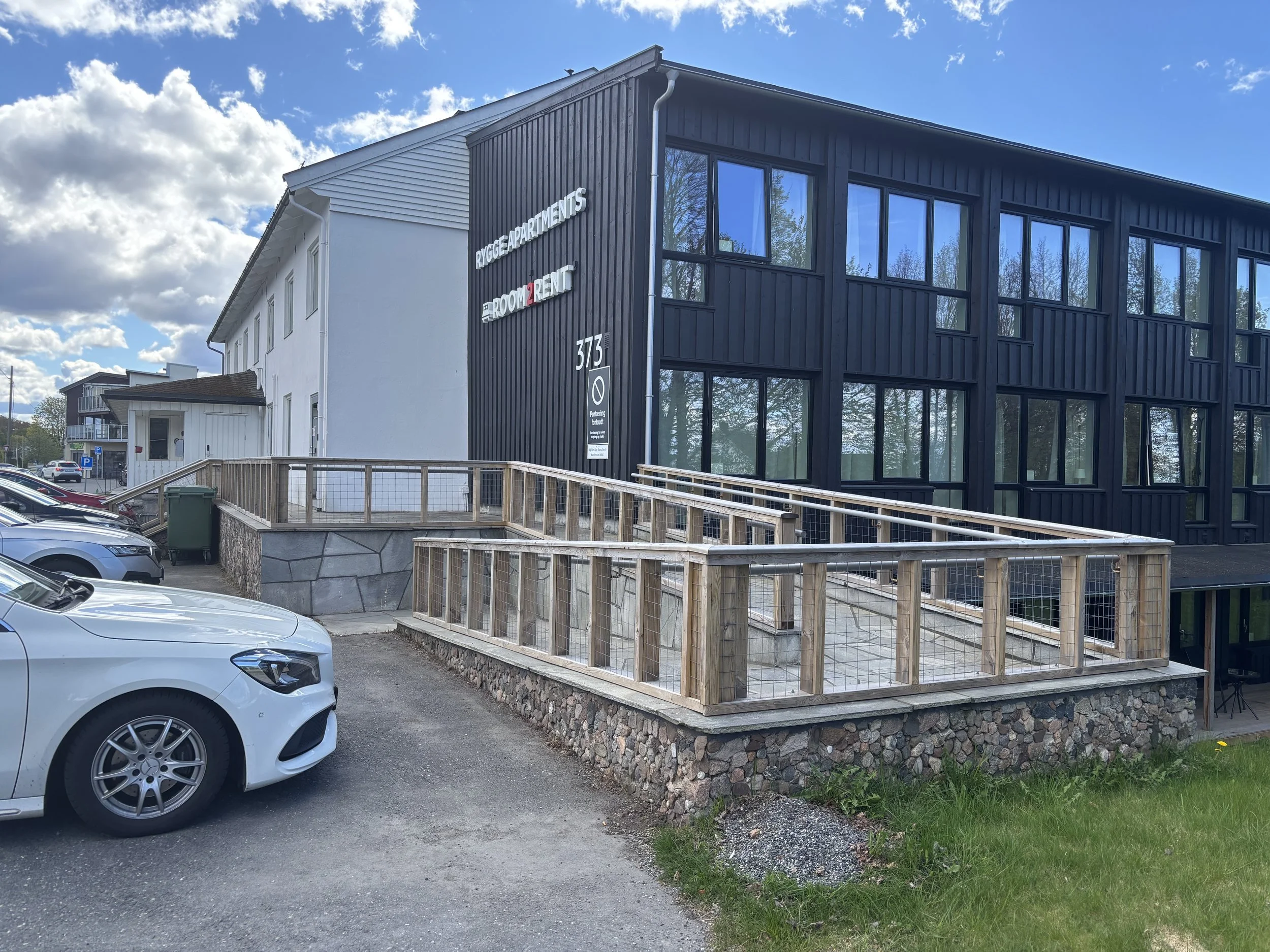 Oversiktsbilde av Rygge Apartments med tilgjengelig rampe i forgrunnen, bygget i tre med metallhåndløpere.