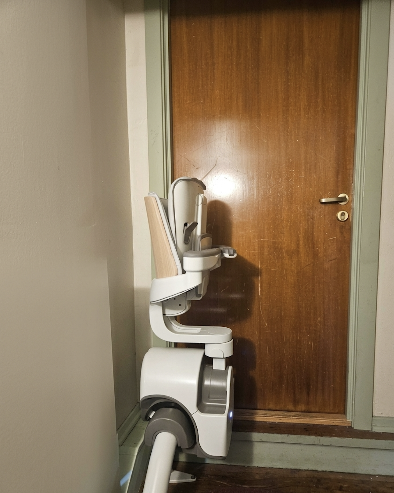 Trappeheis med stolen brettet opp og parkert øverst i trappen foran en tredør. Stolen tar minimalt med plass i oppslått posisjon.