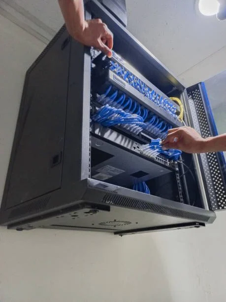 Two people connecting blue Ethernet cables to a network switch inside a server rack.