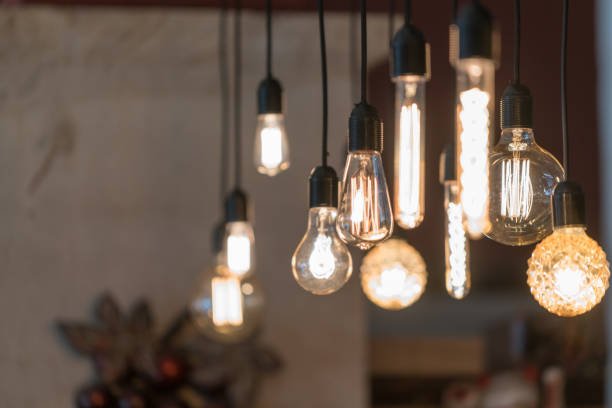 Multiple hanging Edison-style light bulbs with exposed filaments, some glowing, in a warm, cozy interior setting.