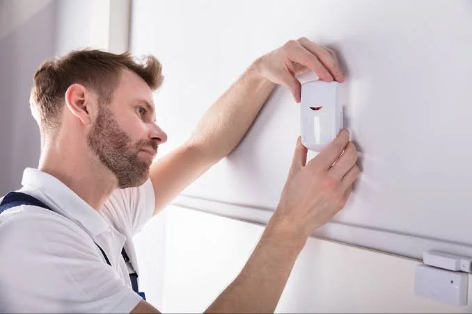 Technician installing a security sensor on a wall.