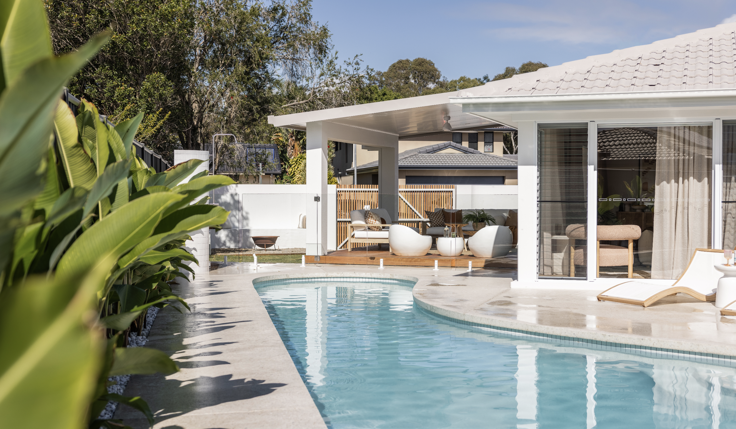 Residential backyard with a swimming pool, patio furniture, and a house with sliding glass doors and curtains.