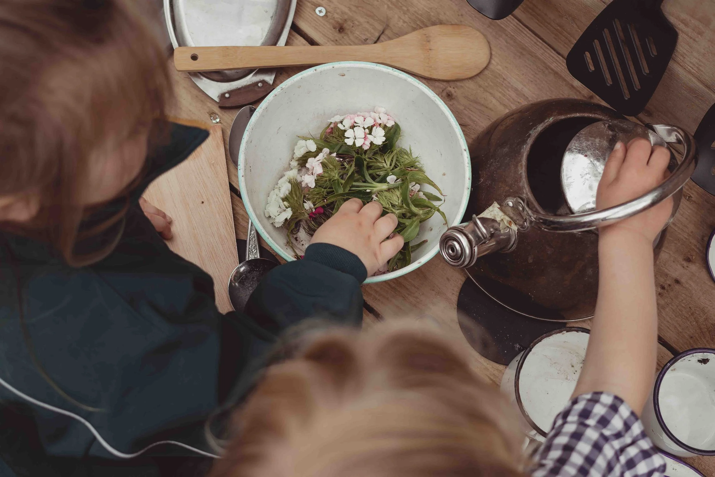 Two children making herbal tea with fresh herbs in a kitchen.