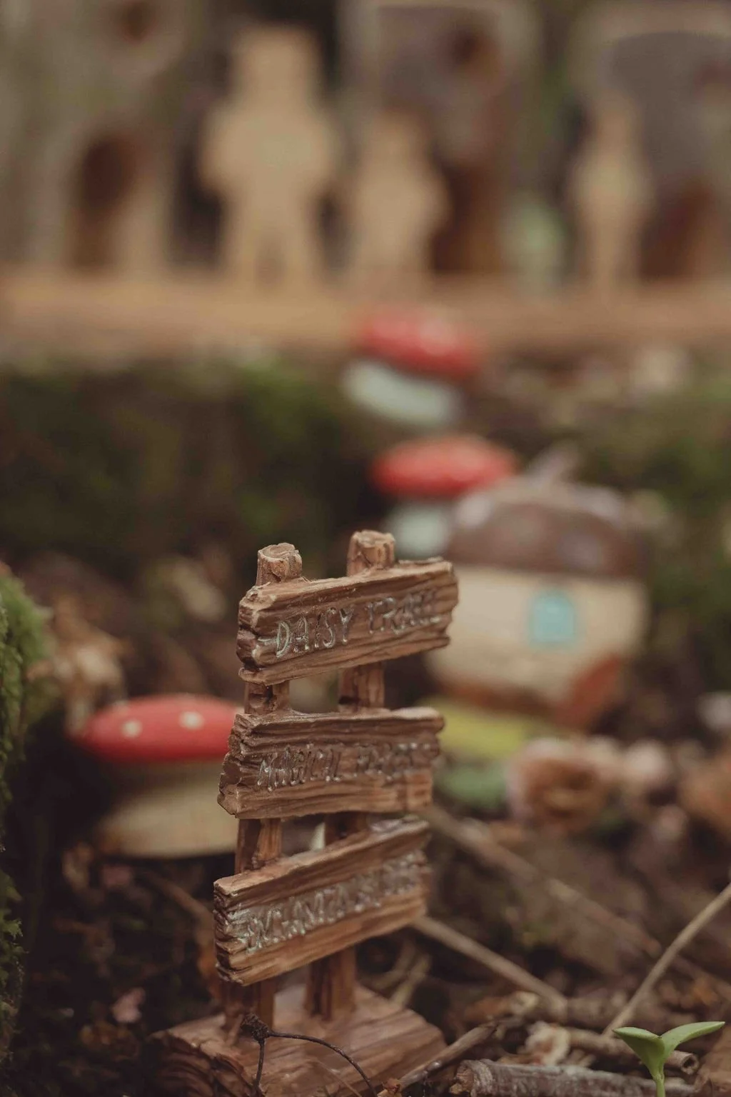 Miniature wooden signpost with text, surrounded by mushrooms and greenery in a miniature garden scene.