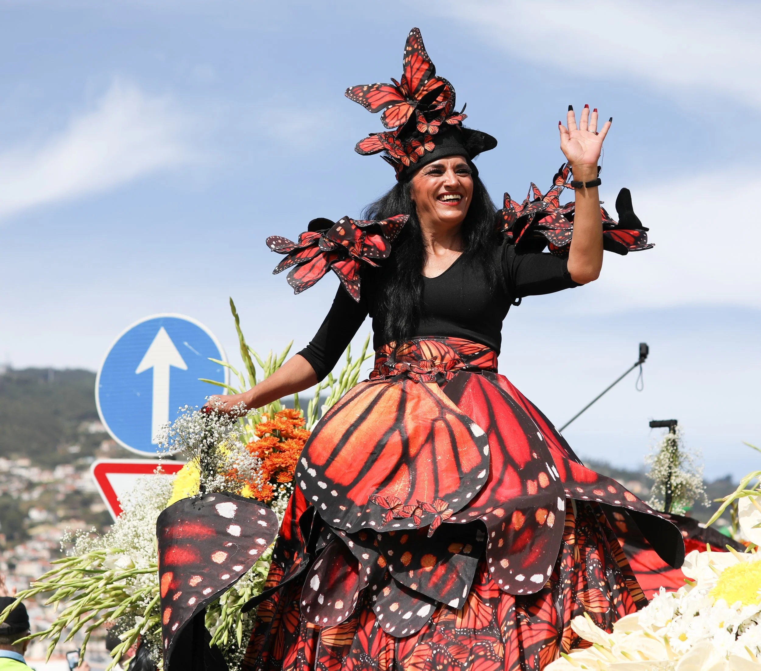 A woman dressed in a butterfly-themed costume, riding on a decorated float with flowers, during a parade or festival.