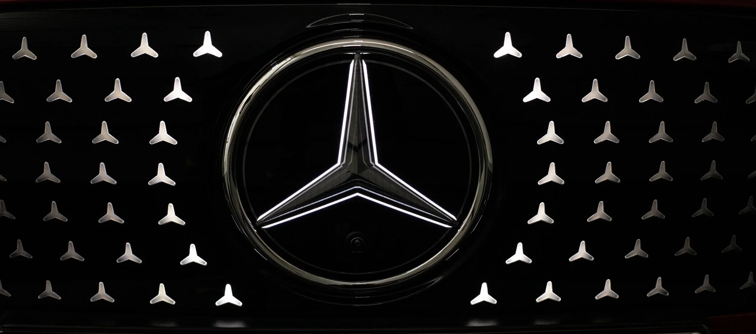 Mercedes-Benz emblem on a black grille with small three-pointed star designs.