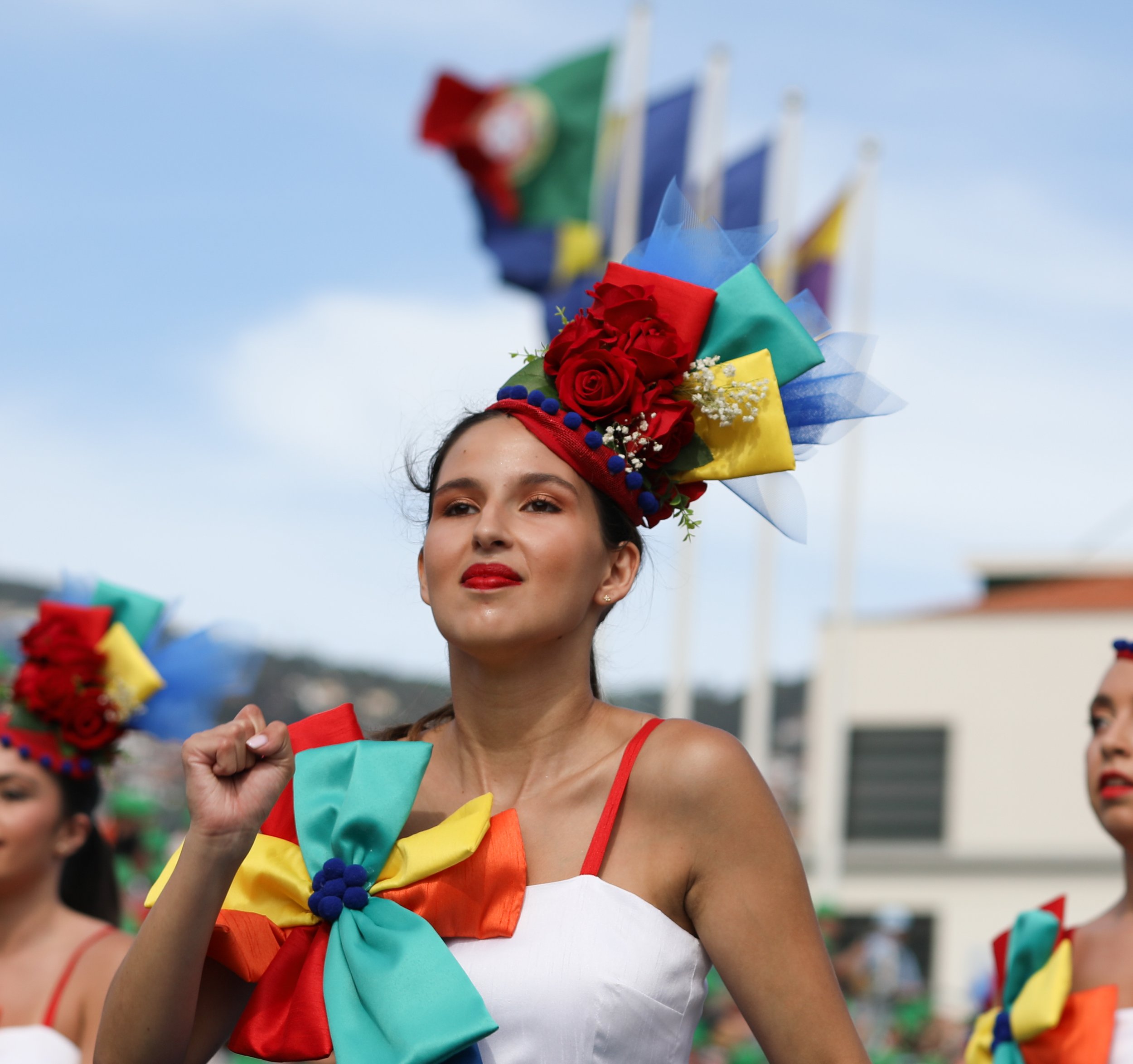 A woman wearing a colorful flower and ribbon headpiece, with a bow on her chest, participating in a festive parade.