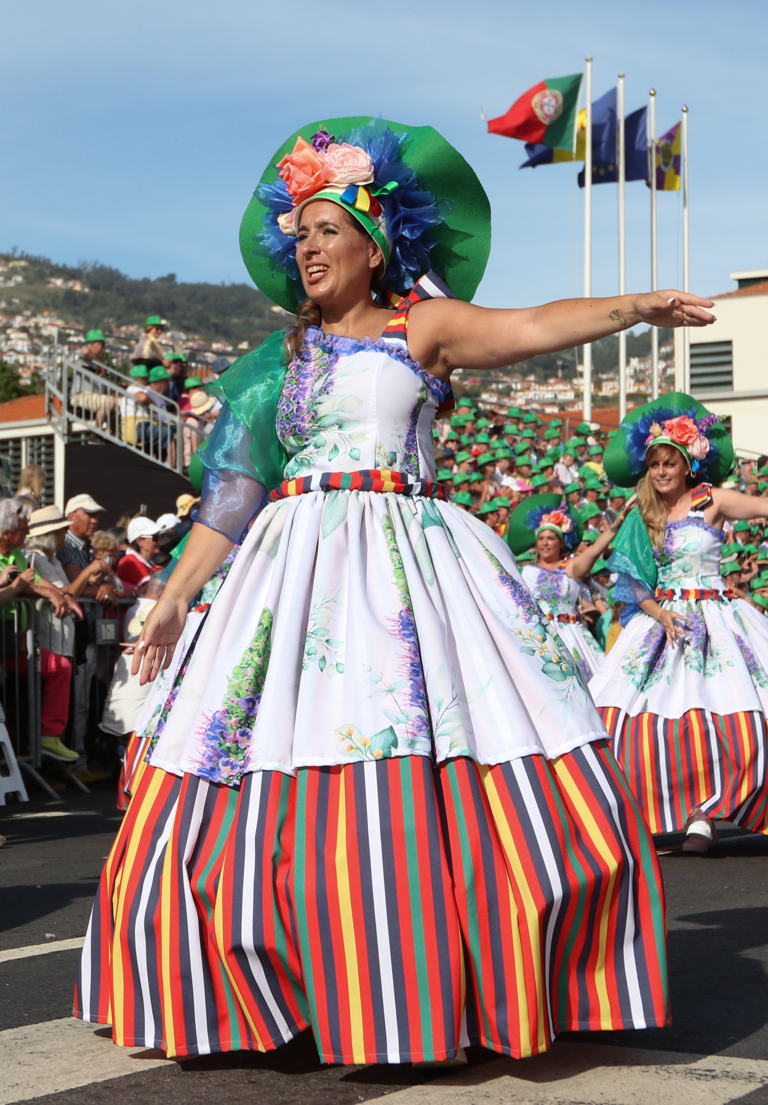 Women in colorful costumes participating in a parade, with flags in the background.