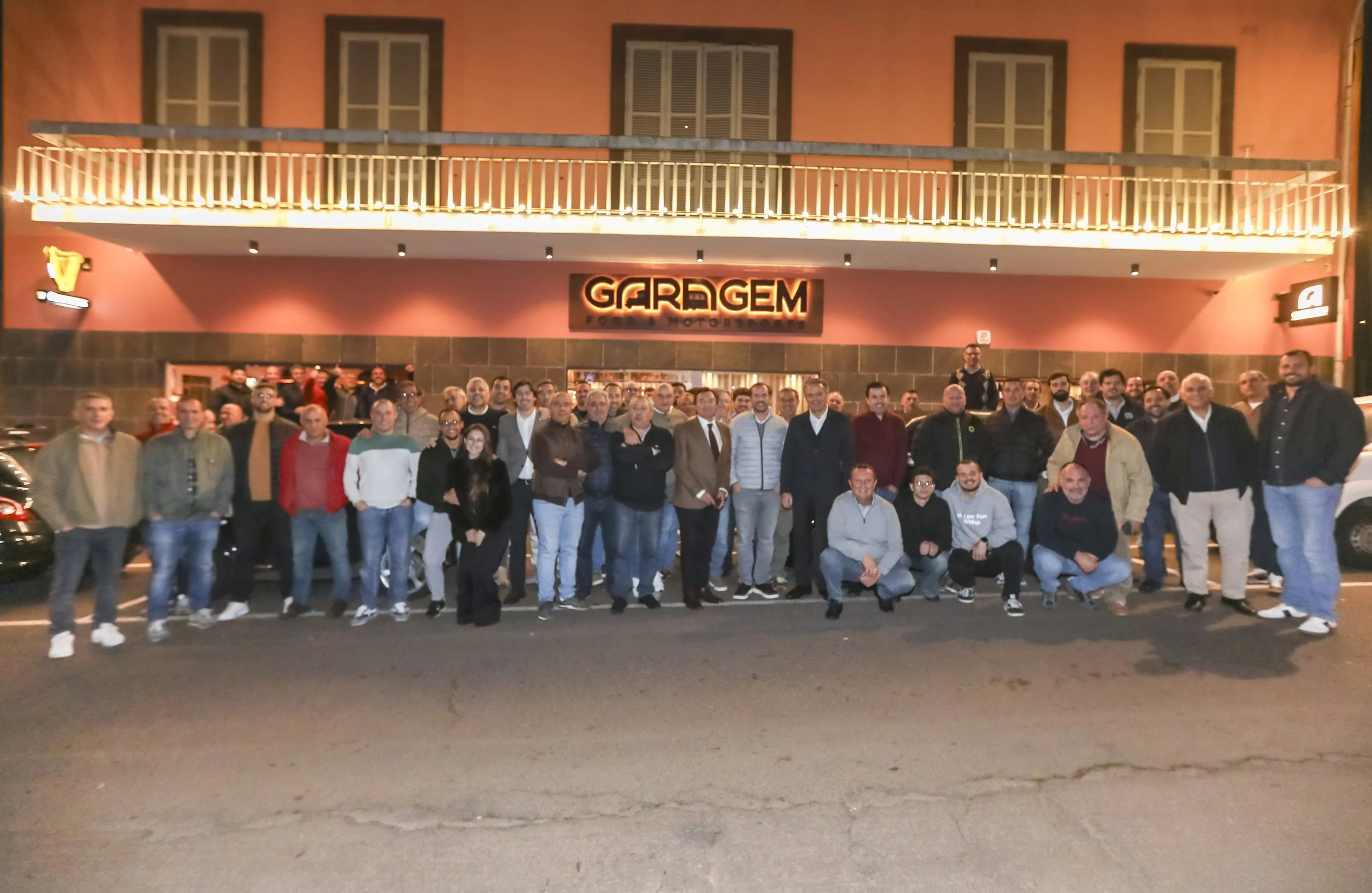 Group of people standing outside a building at night, with a sign that reads 'GARGEM' on the wall behind them.