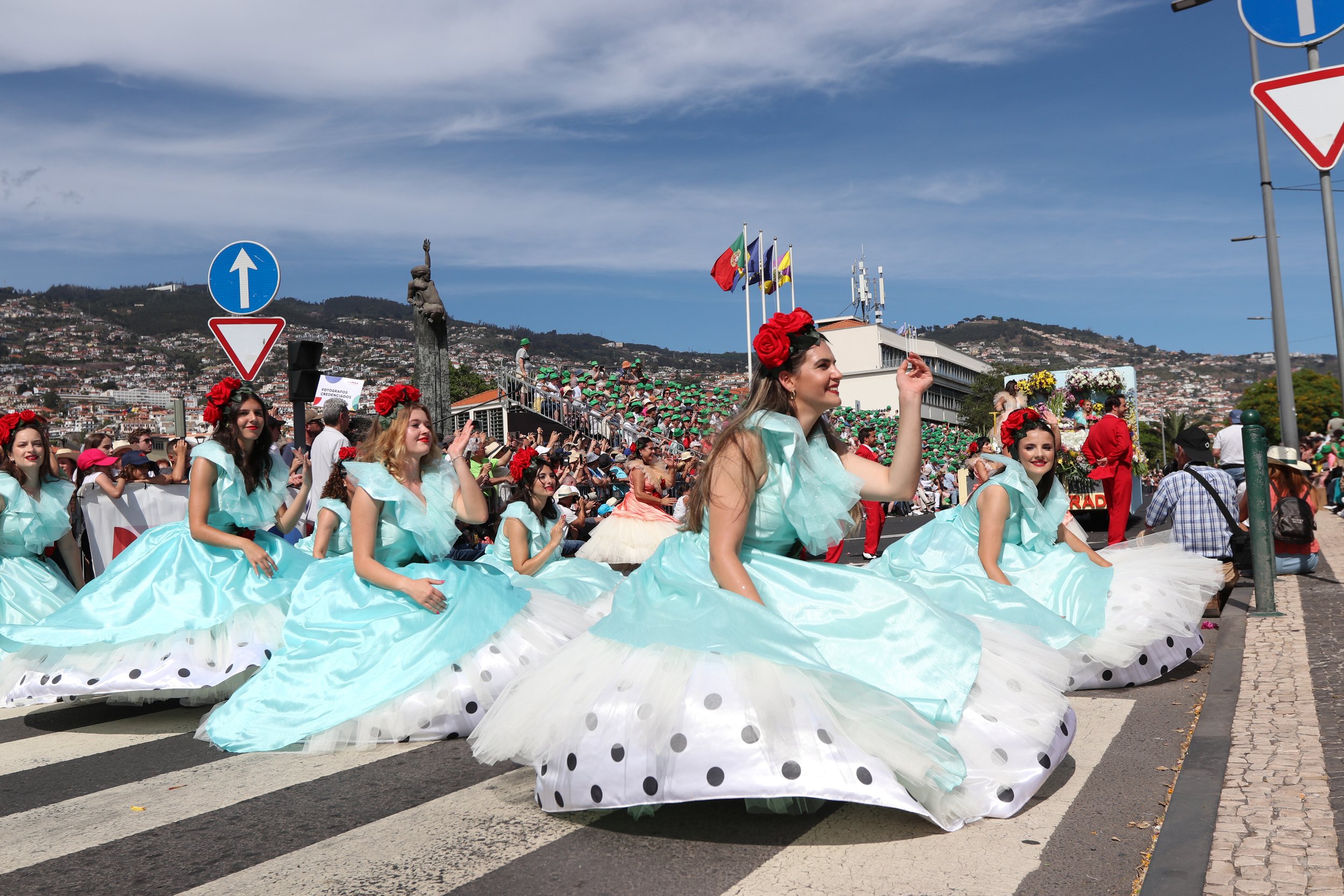 Women in colorful dresses with flower headbands participating in a parade.