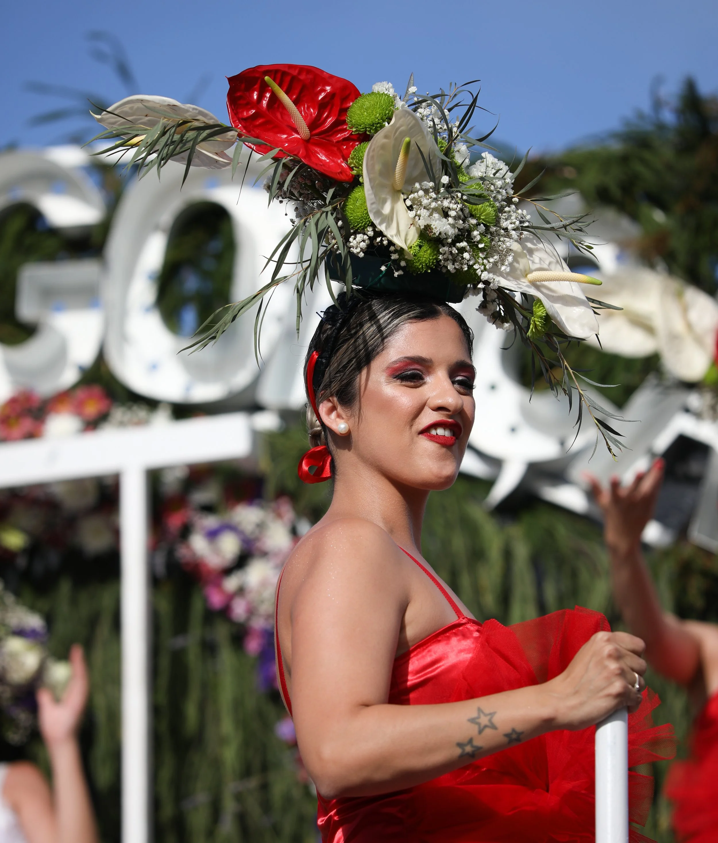 Woman wearing a red dress and an elaborate floral headpiece during a parade or celebration.