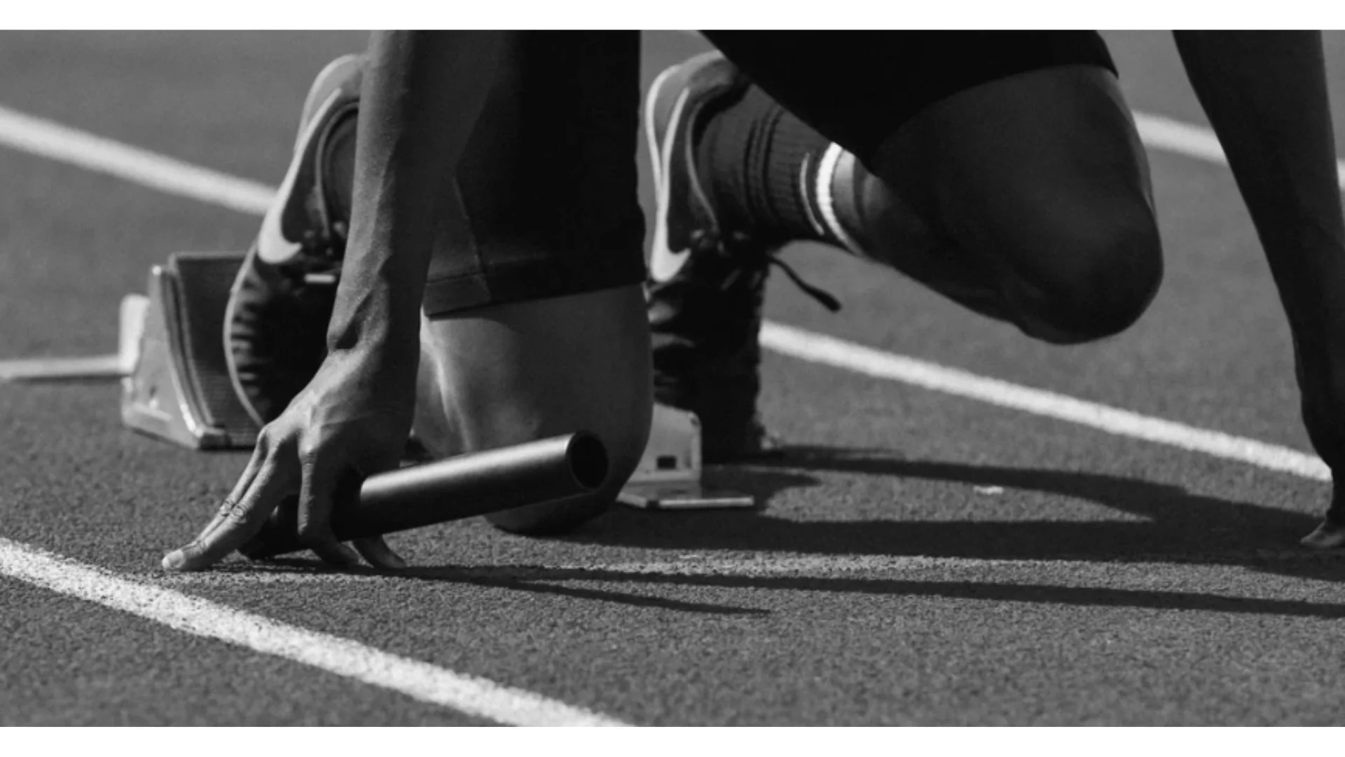 Eine schwarze Silhouette einer Person in Startposition auf einer Laufbahn, bereit zum Sprinten, in Schwarz-Weiß-Aufnahme.