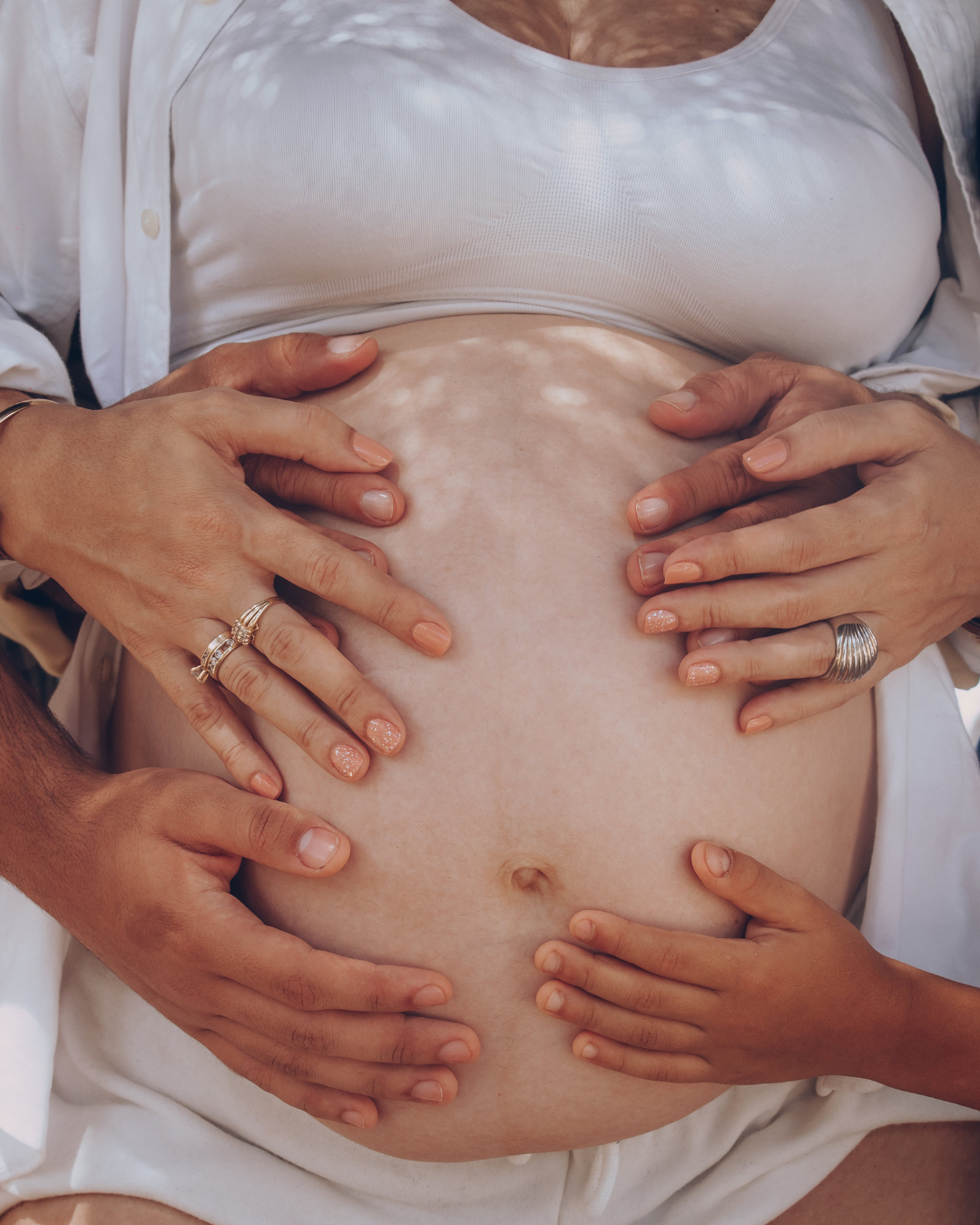 Multiple hands gently holding a pregnant woman's belly.