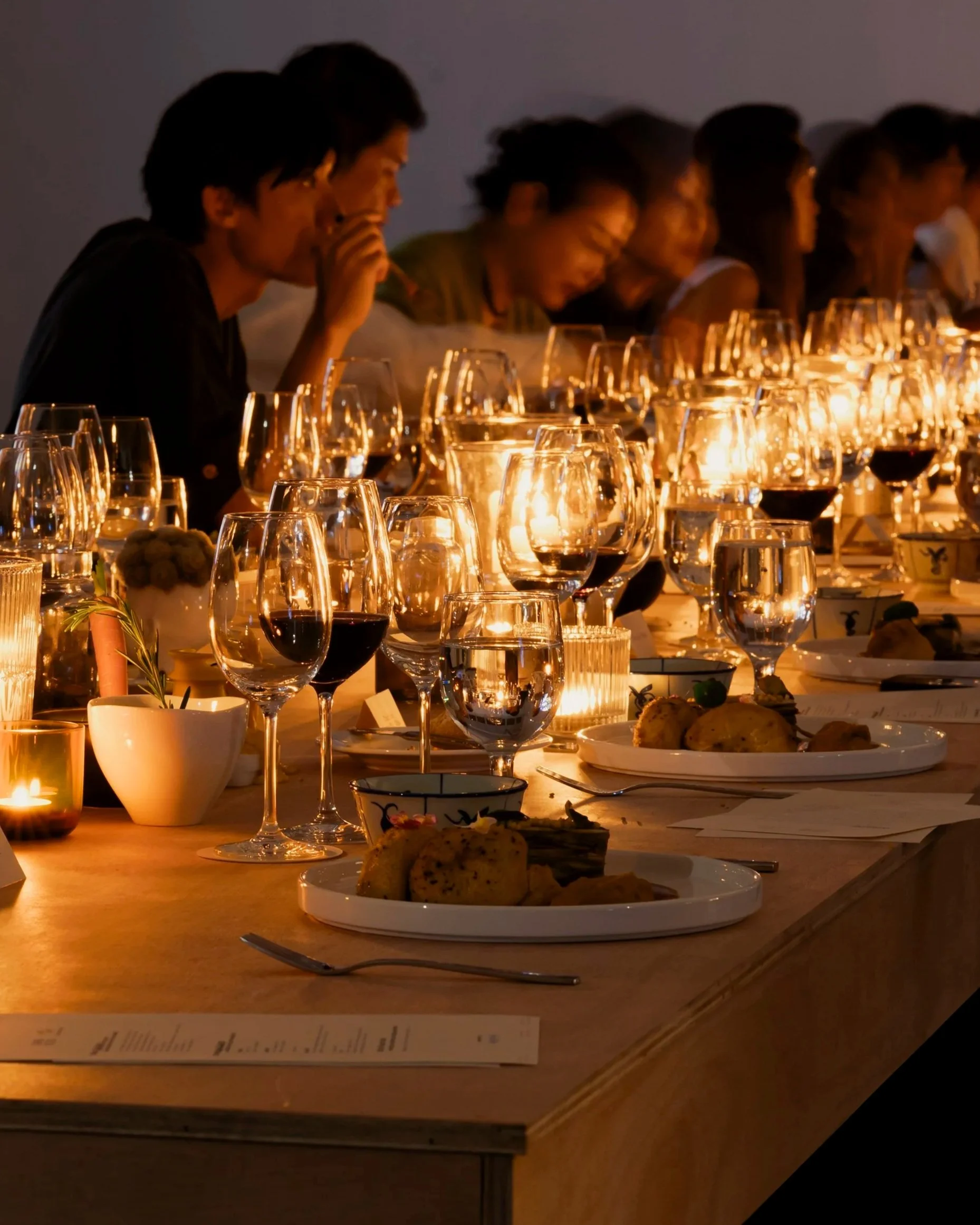 People dining at a candlelit dinner table, with glasses of wine and plates of food.