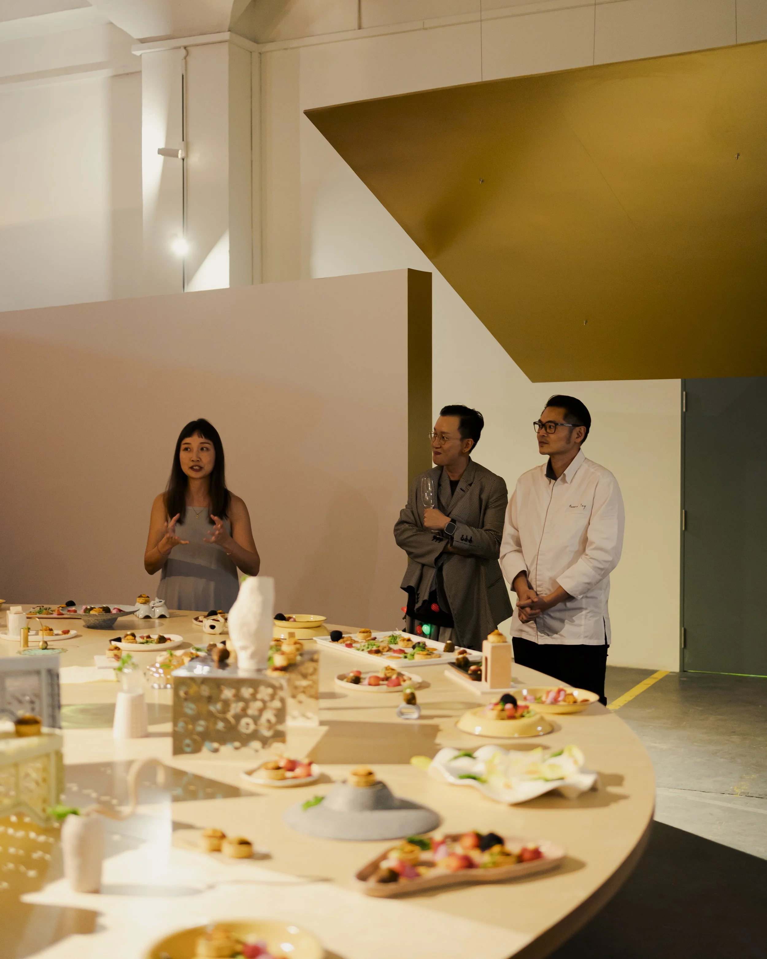 People standing around a table with assorted desserts in a modern, well-lit interior space.