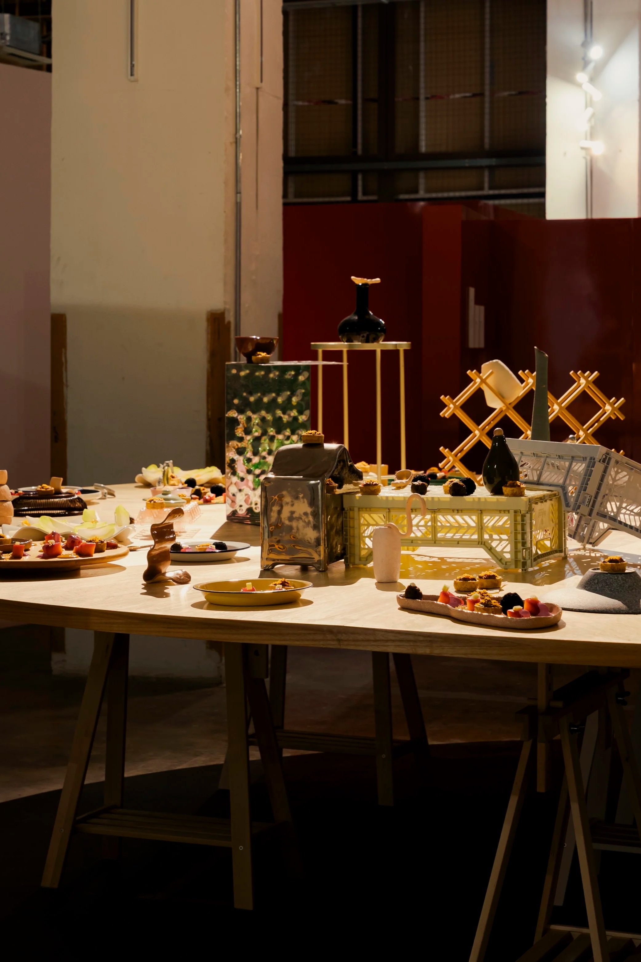 A table with various small artistic and decorative objects, including plates with colorful items, set against an indoor background with warm lighting.