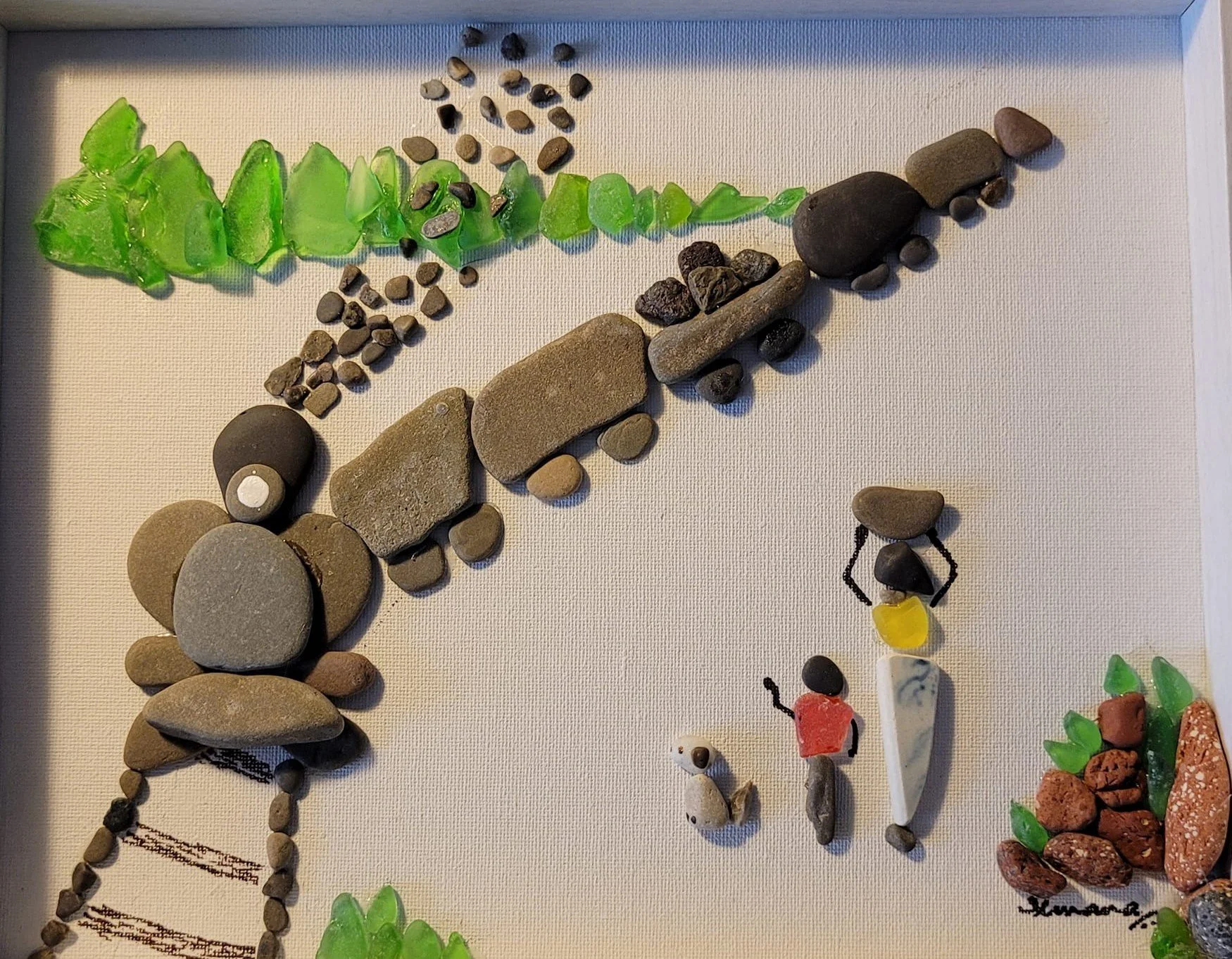 A train made of pebbles passes by a village, as a woman, her daughter and a dog, on their way back, watch it pass by.