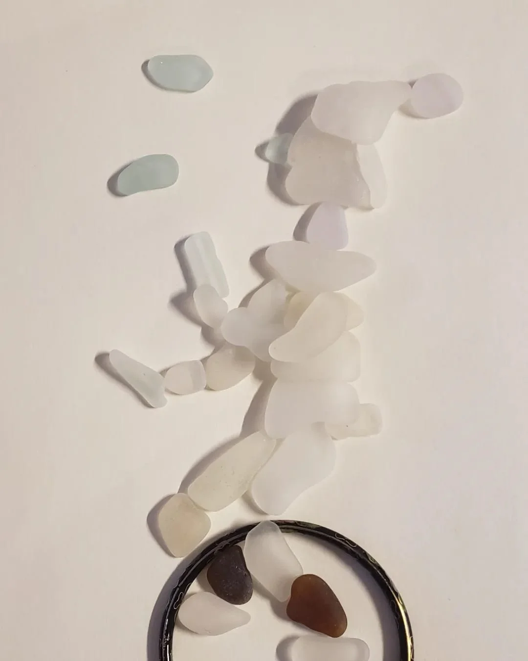 A collection of various white sea glass and and a bangle on a canvas board depicting how the creative process begins.