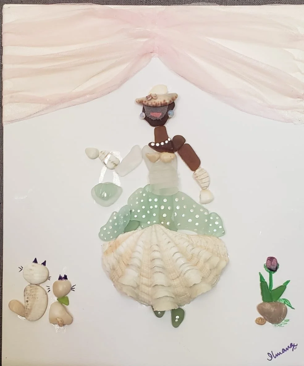 Artwork of a woman made from seashells, with a black face, wearing a hat, pearl earrings, pearl necklace, green polka dot skirt, and yellow seashell shoes, standing under pink curtain, with two shell cats and a shell potted plant with a pink flower beside her.