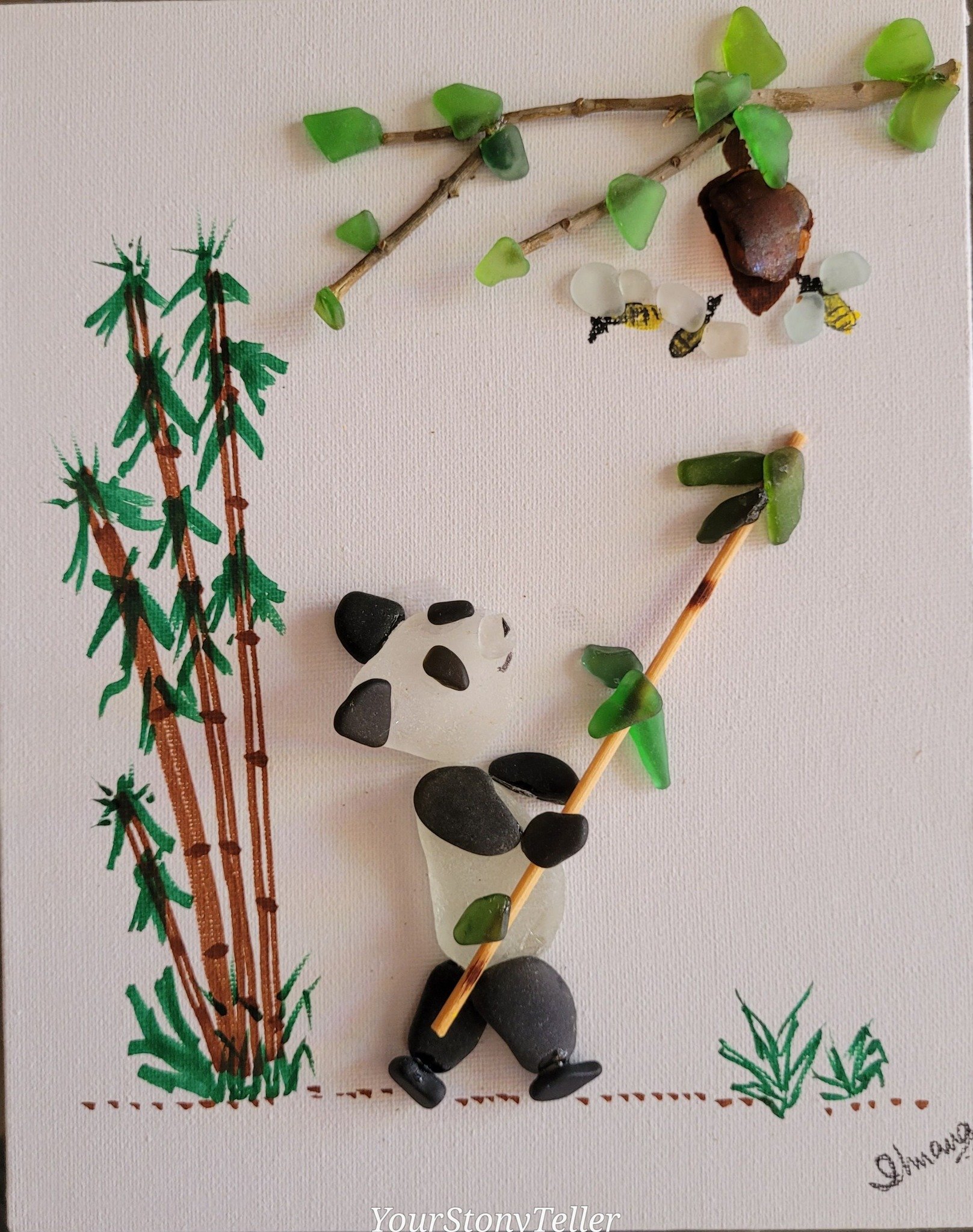 Artistic collage of a panda holding bamboo, made from rocks, sticks, and sea glass, with drawn bamboo trees on a paper background.