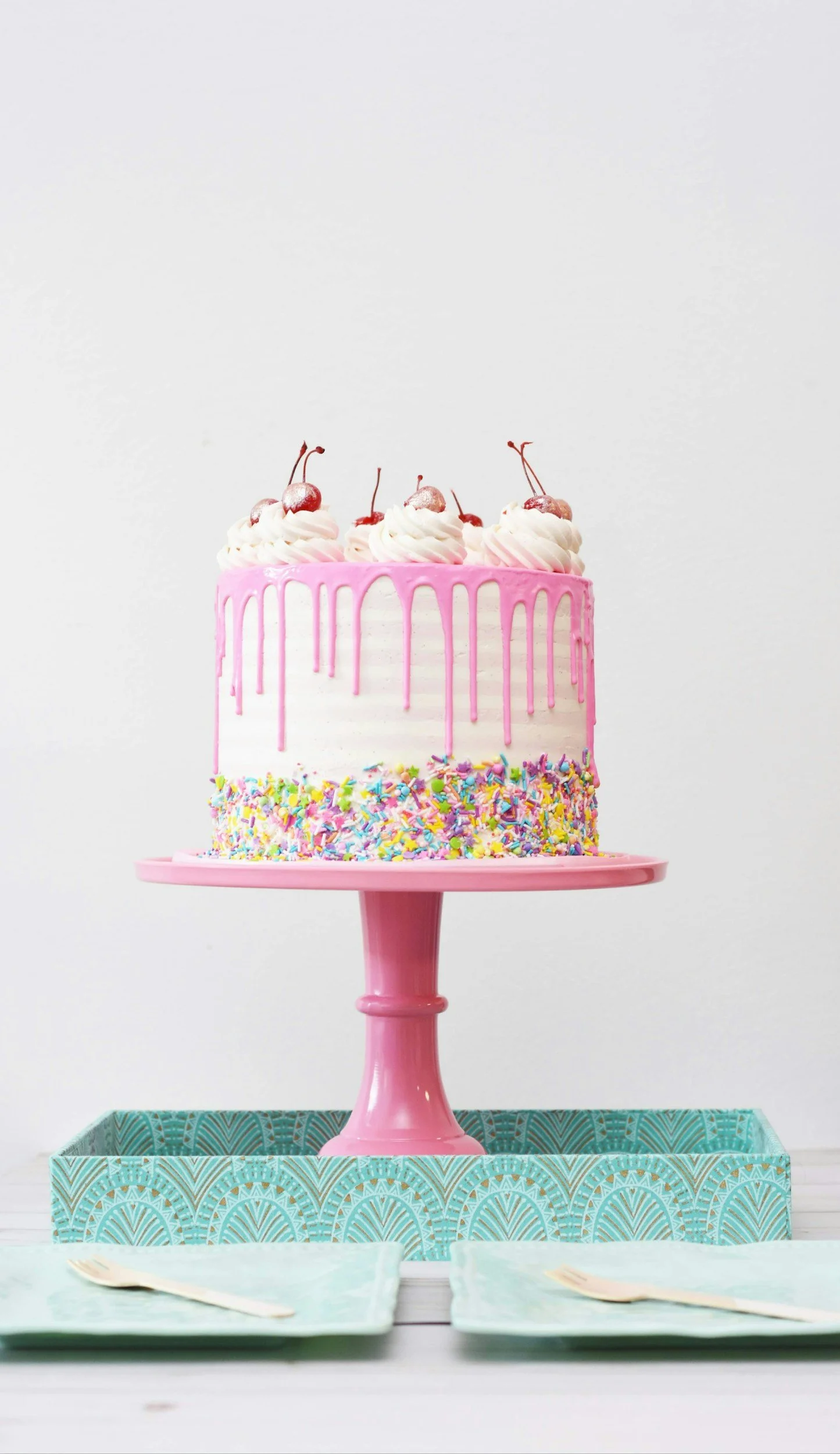 Ein bunter Geburtstagskuchen mit pinkem Zuckerguss, bunten Streuseln und Sahne mit Kirschen, auf einem pinken Tortenständer