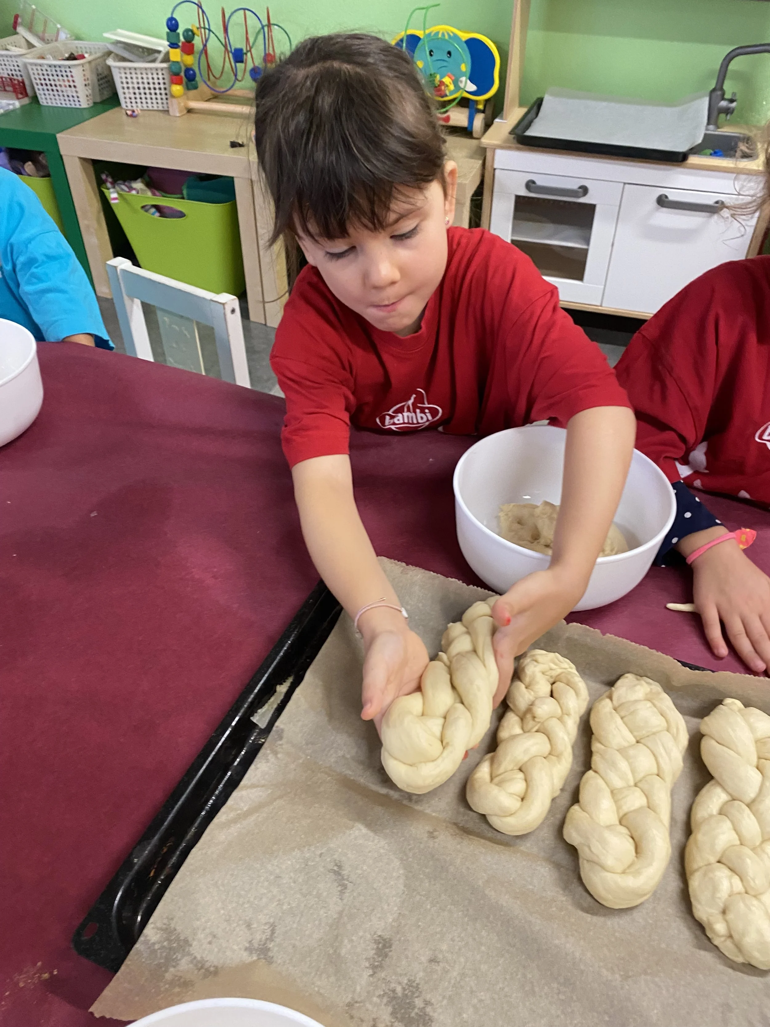 Ein Kind, das Teig zu Zöpfen flechtet, während es in einer Küche oder im Kindergarten aktiv ist.