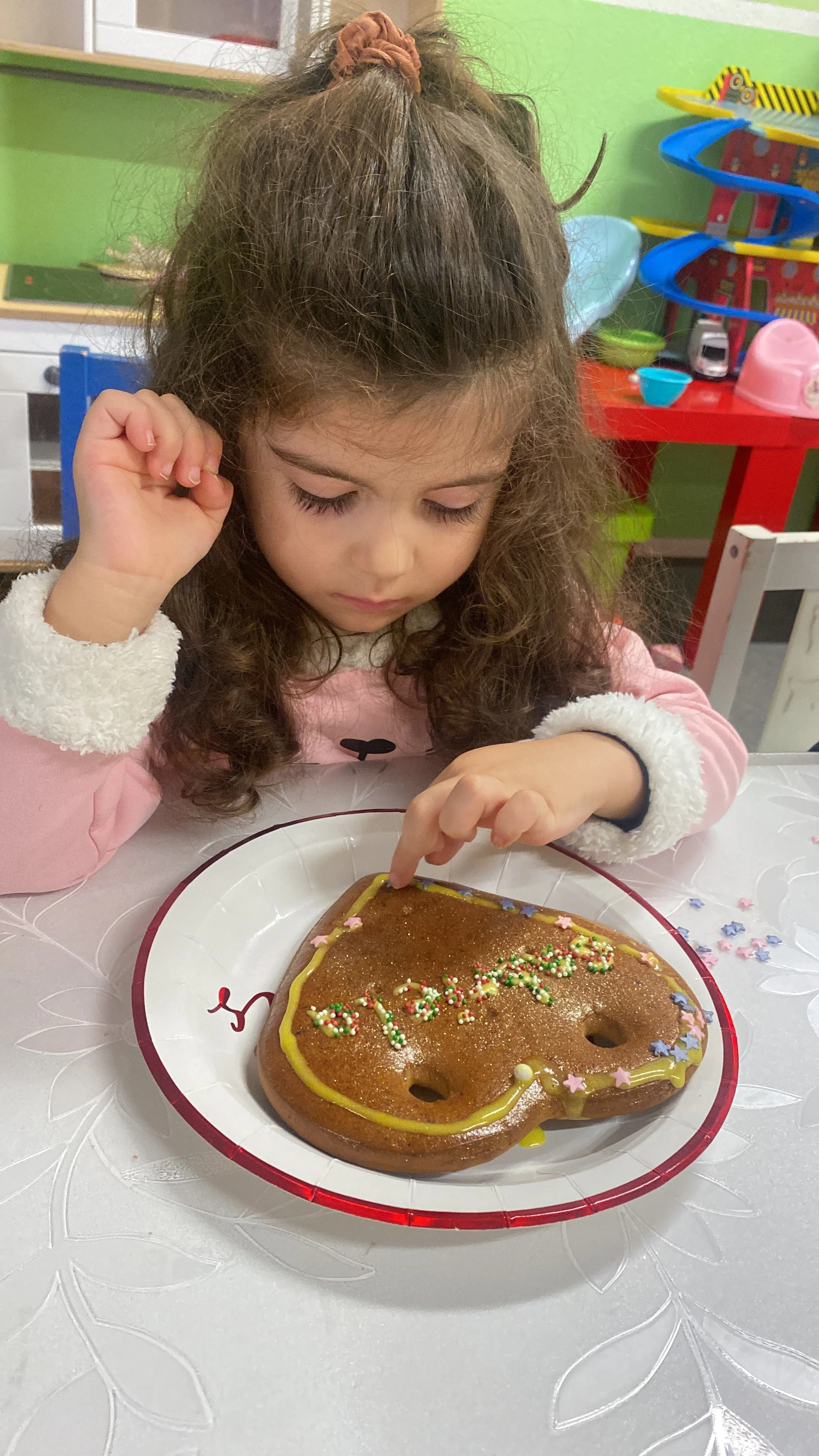 Ein Mädchen mit lockigem Haar, das eine Geburtstagstorte in Form eines Bären auf einem Teller dekoriert.