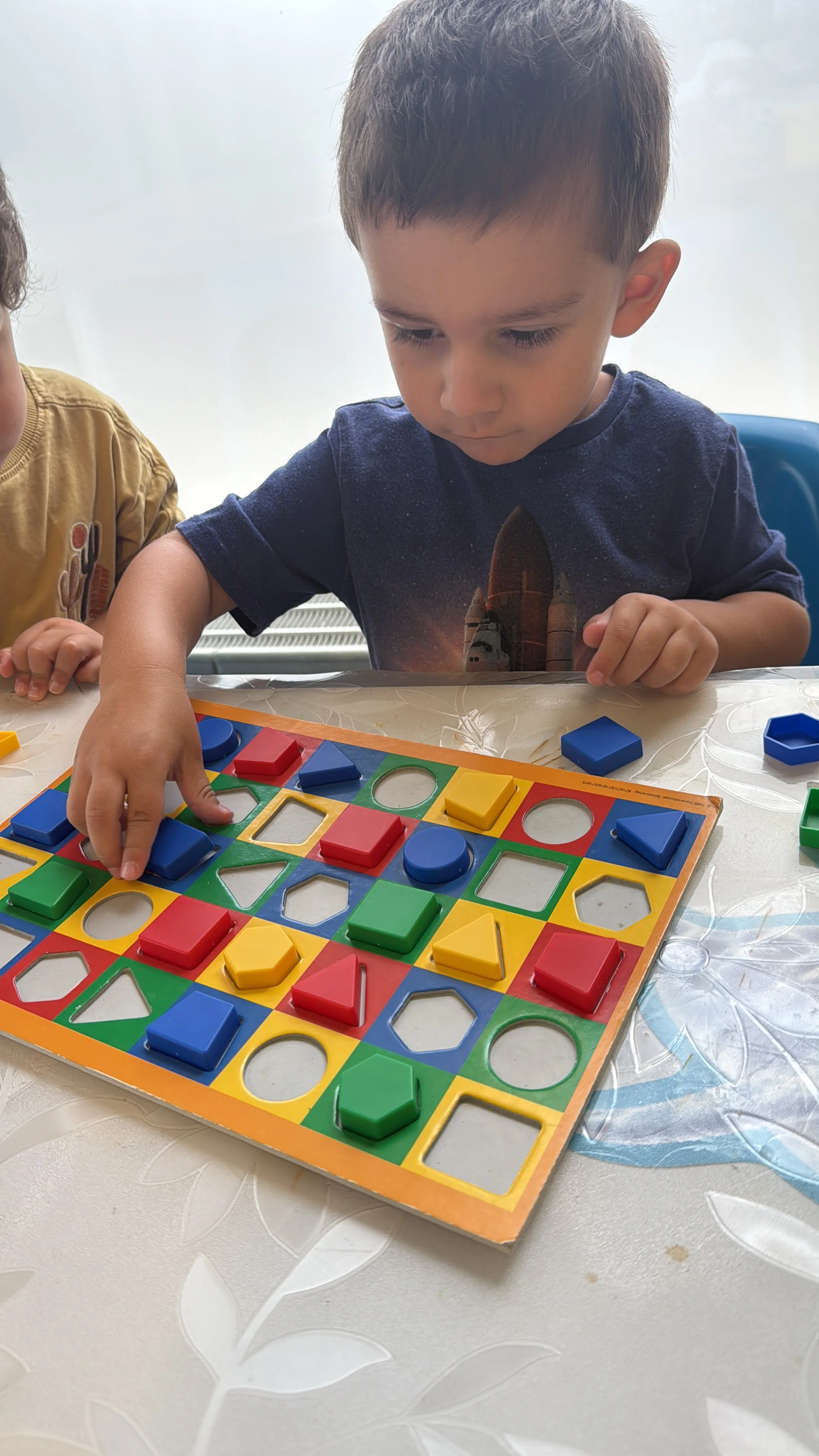 Ein kleiner Junge spielt mit einem bunten Gesellschaftsspiel auf einem Tisch.