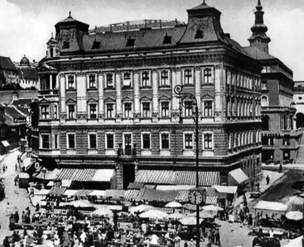 Black and white photo of a historical multi-story building with market stalls and umbrellas in the foreground.