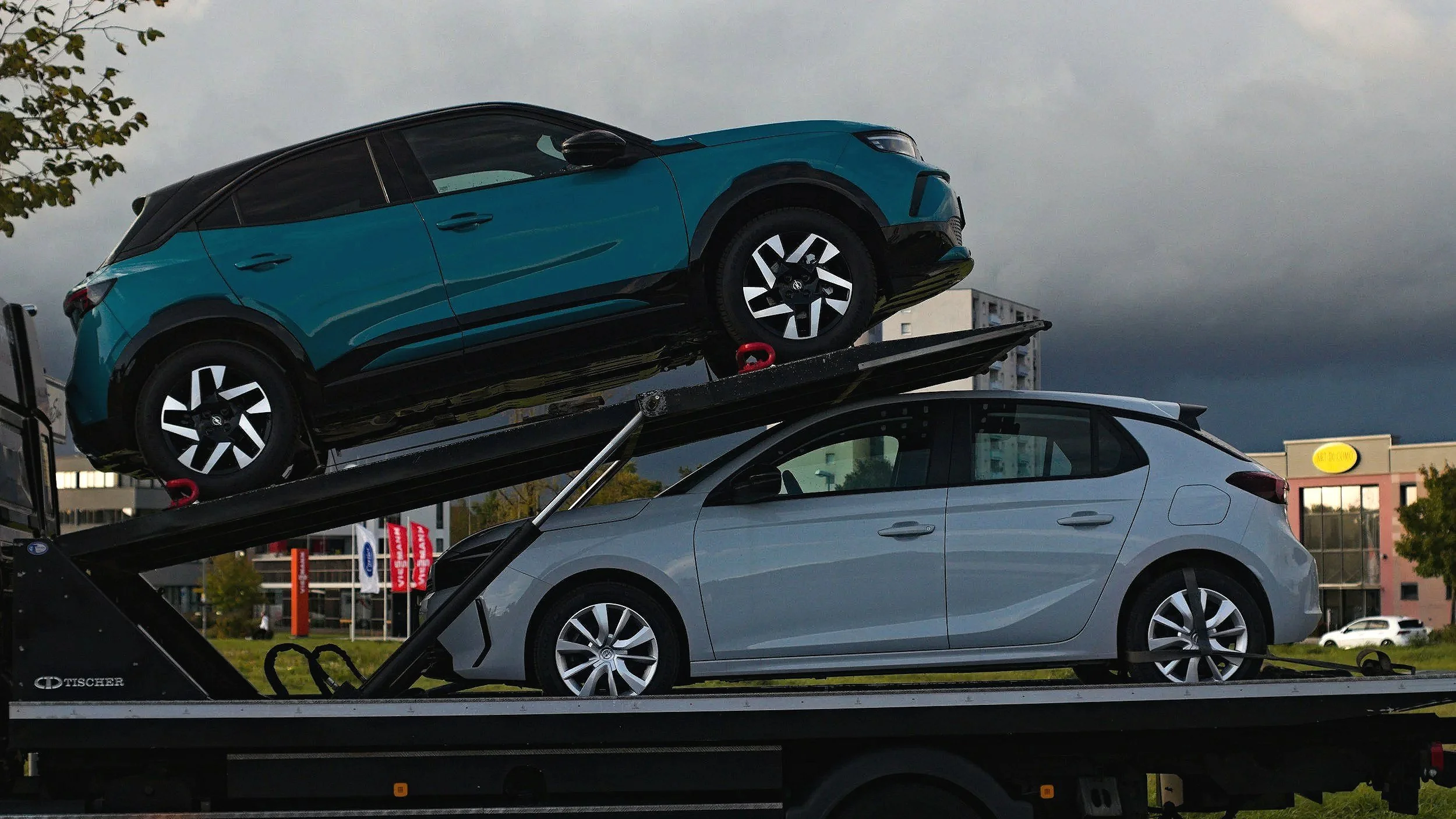 Carro de cor azul escura sendo transportado em uma carreta. O carro está estacionado na parte superior da carreta.